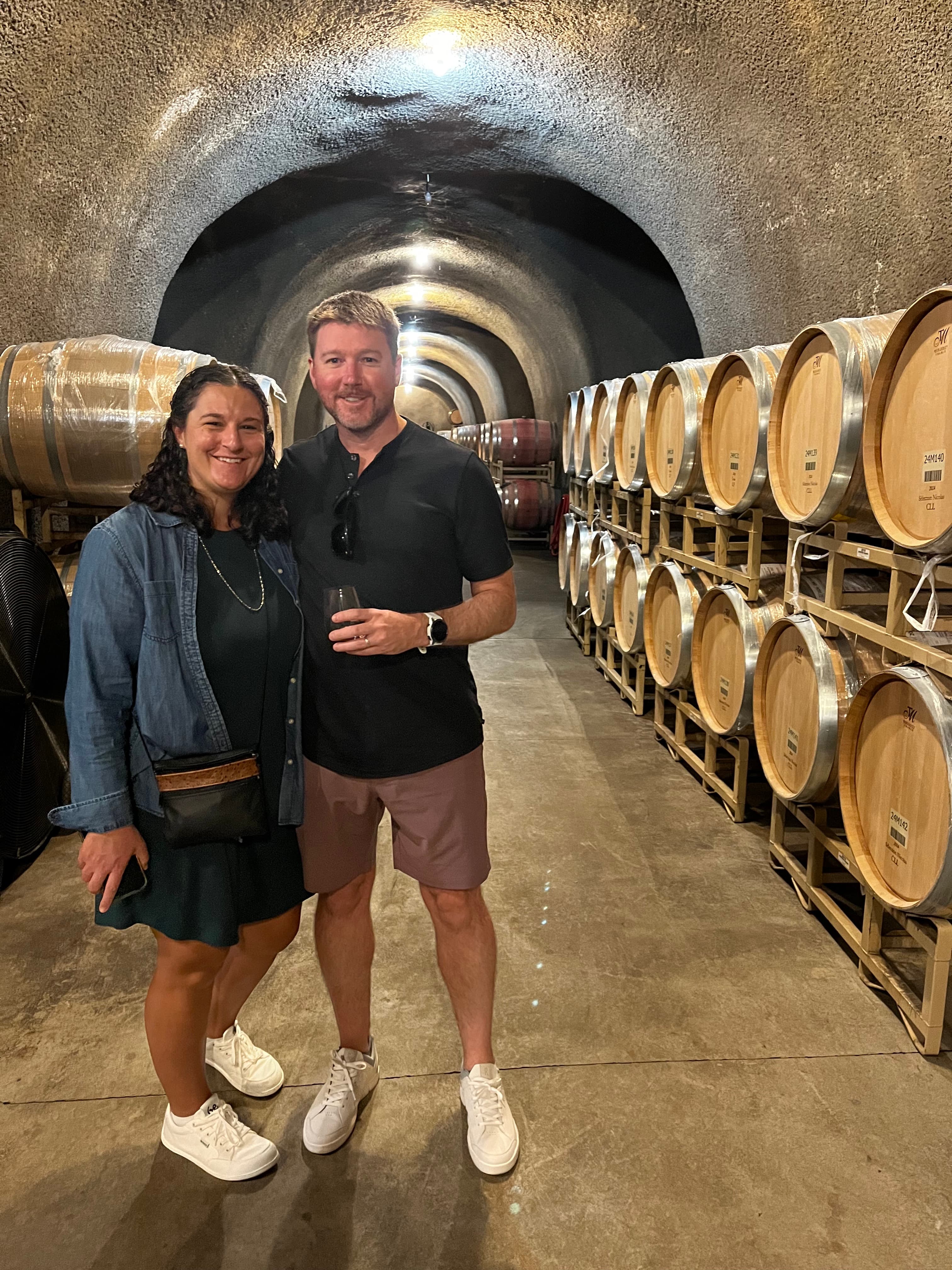 Advisor and partner smiling side by side in a cellar with rows of barrels