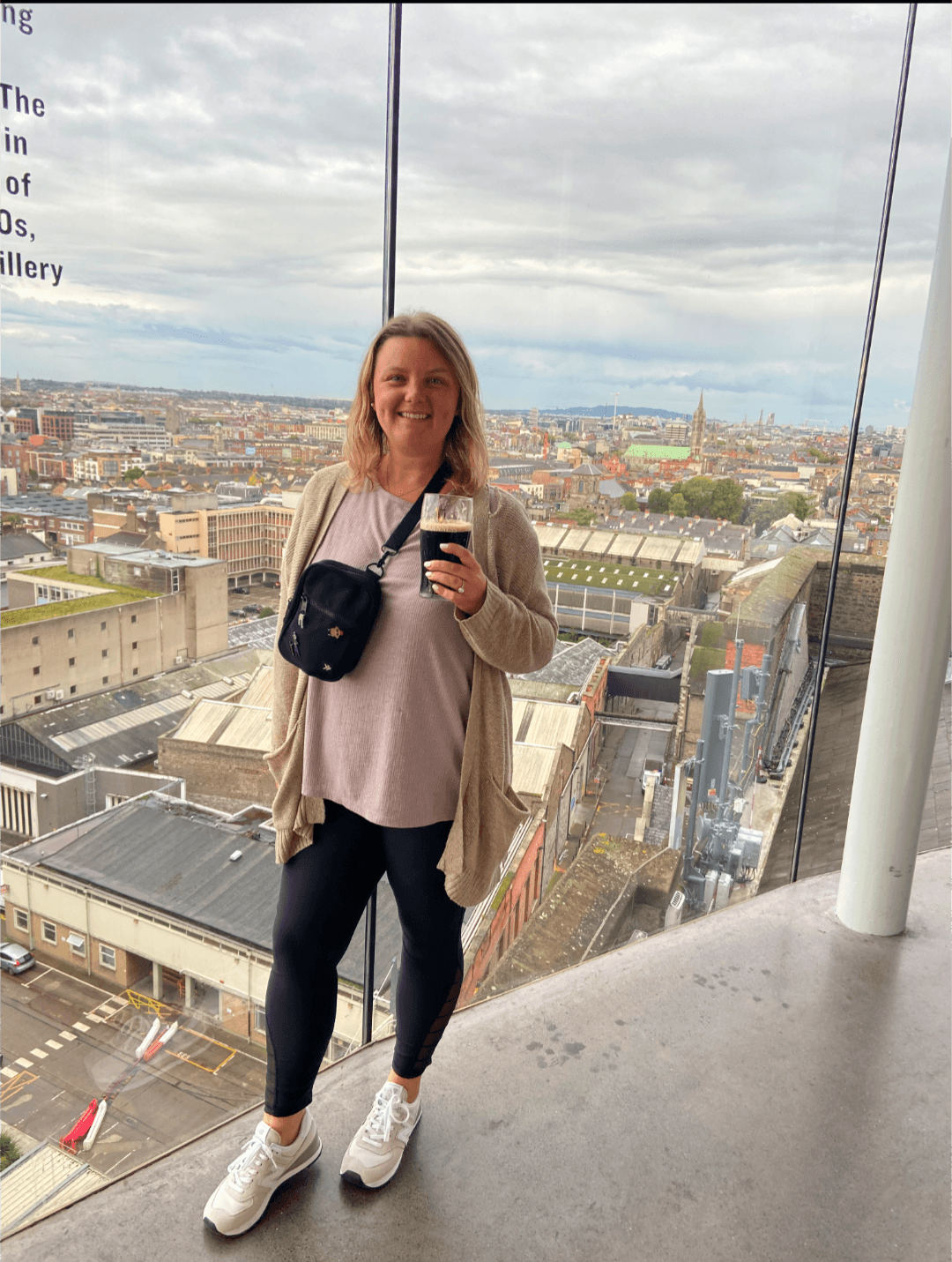 Advisor holding a glass of Guinness in front of floor-to-ceiling glass windows overlooking Dublin on a cloudy day