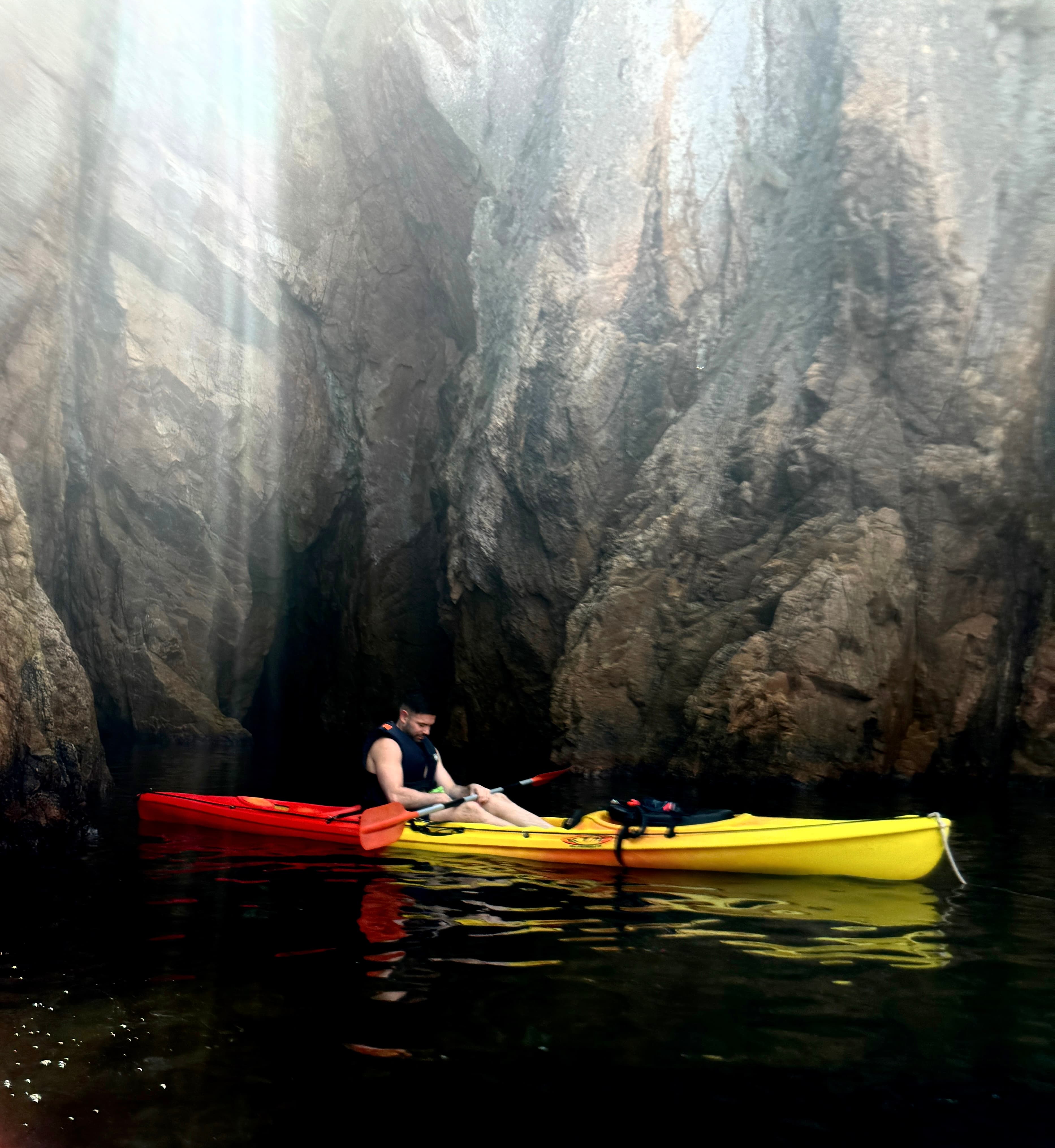 Advisor in a red and yellow kayak on the water below dramatic cliffs