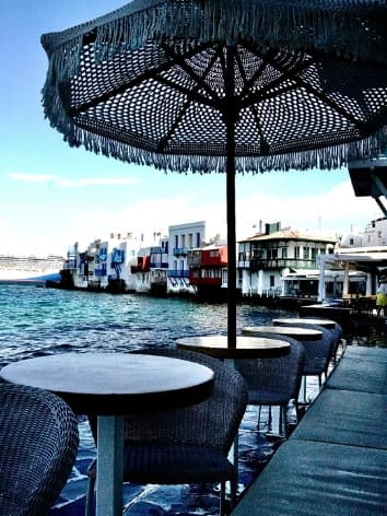 View of a row of small circular tables by the sea under an umbrella during the day