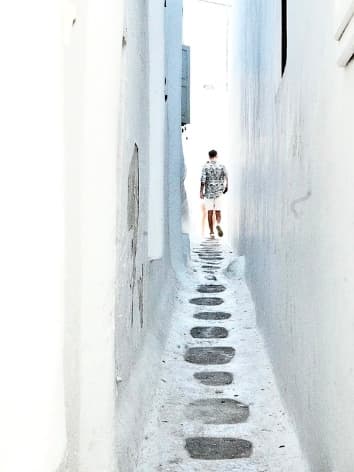 View of a narrow stone path between white buildings with a person visible at the end