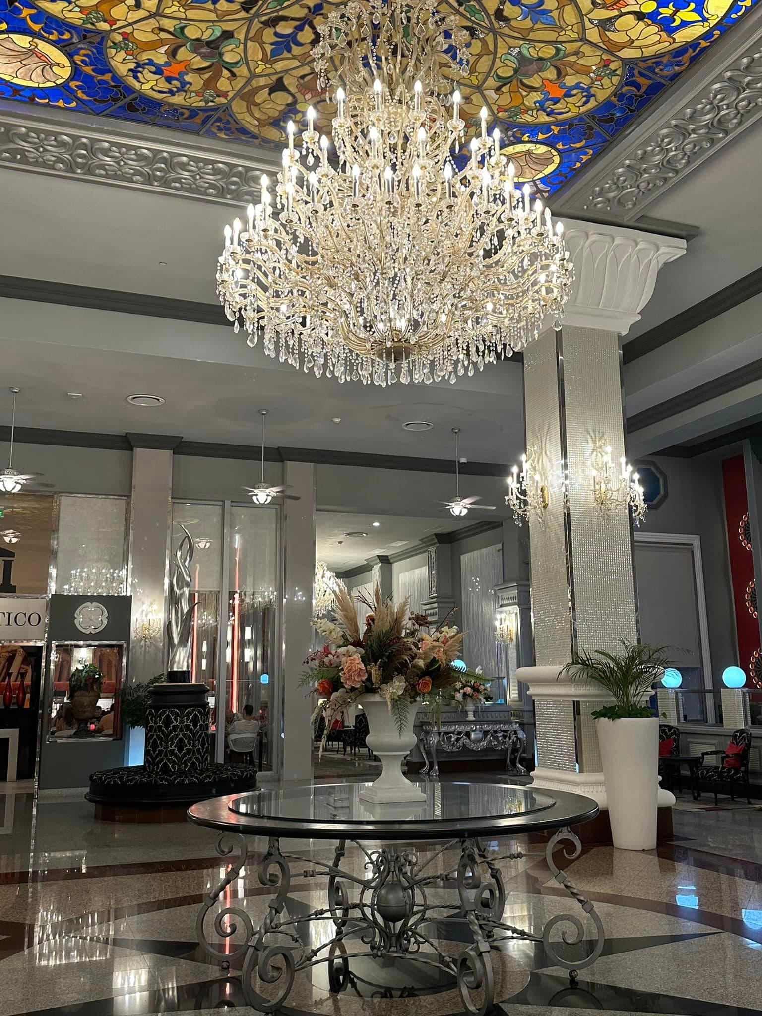 Interior view of a grand lobby with large crystal chandelier hanging above a glass table