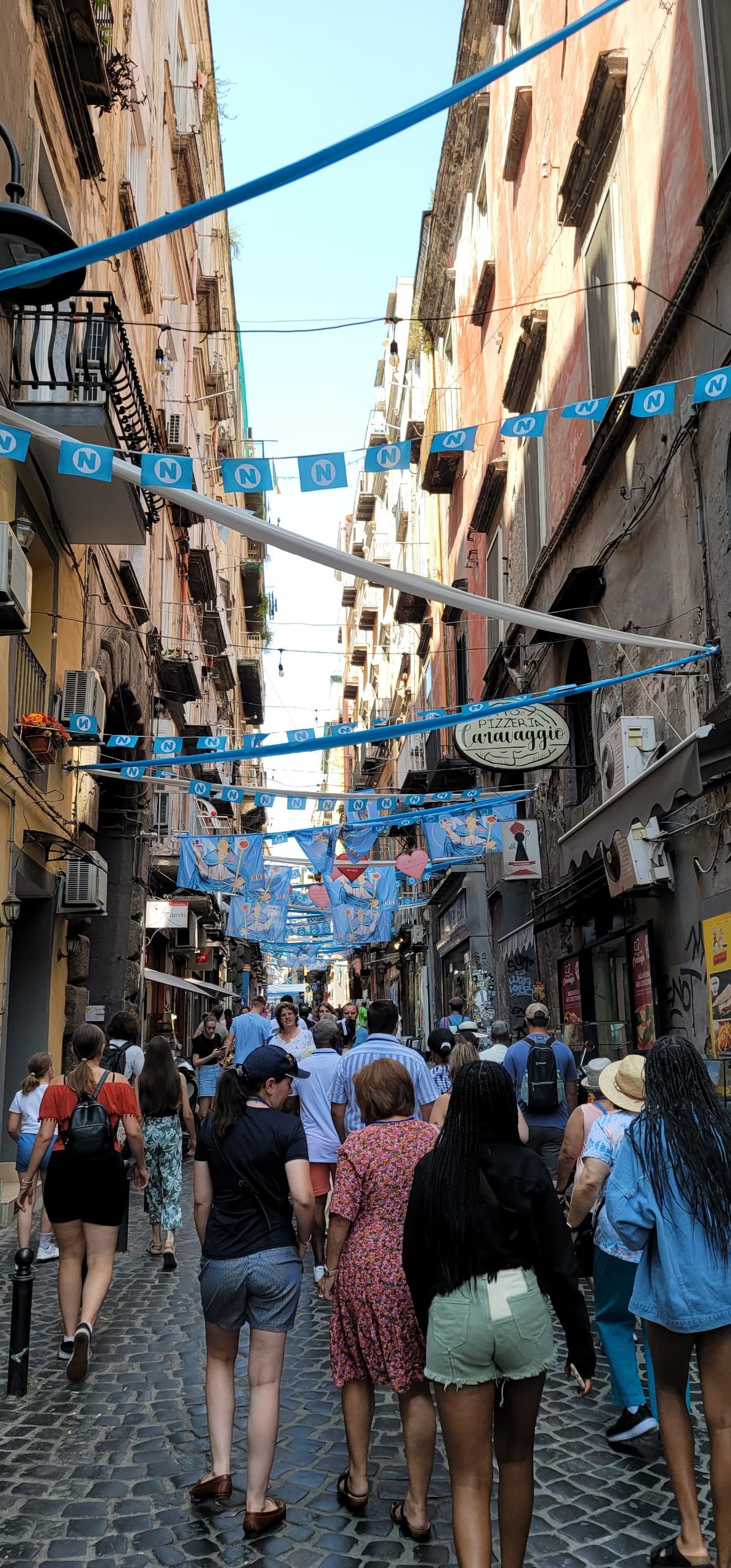 View of pedestrians walking along a crowded street with small blue flags hanging in rows overhead