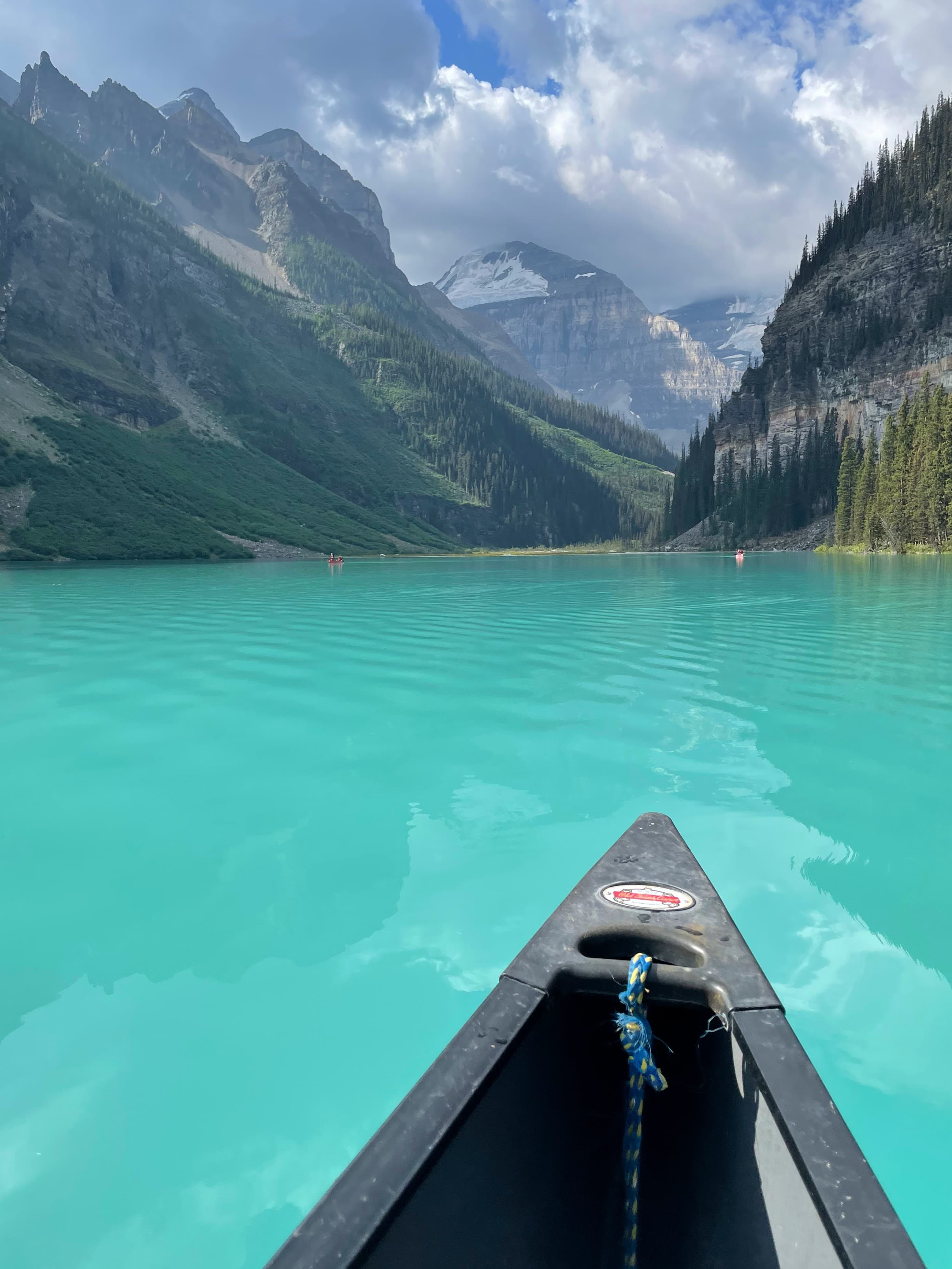 The front of a small boat visible on a bright blue glacial lake in the midst of large mountains