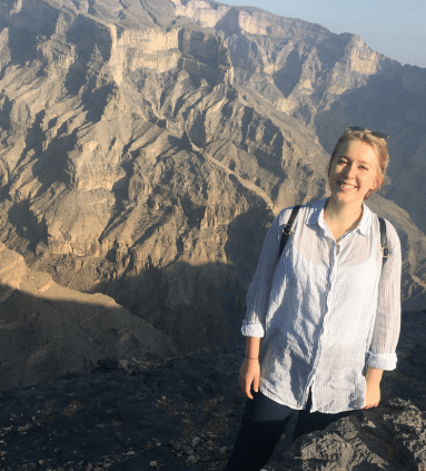 Advisor smiling on a hike overlooking a dramatic mountain range on a sunny day