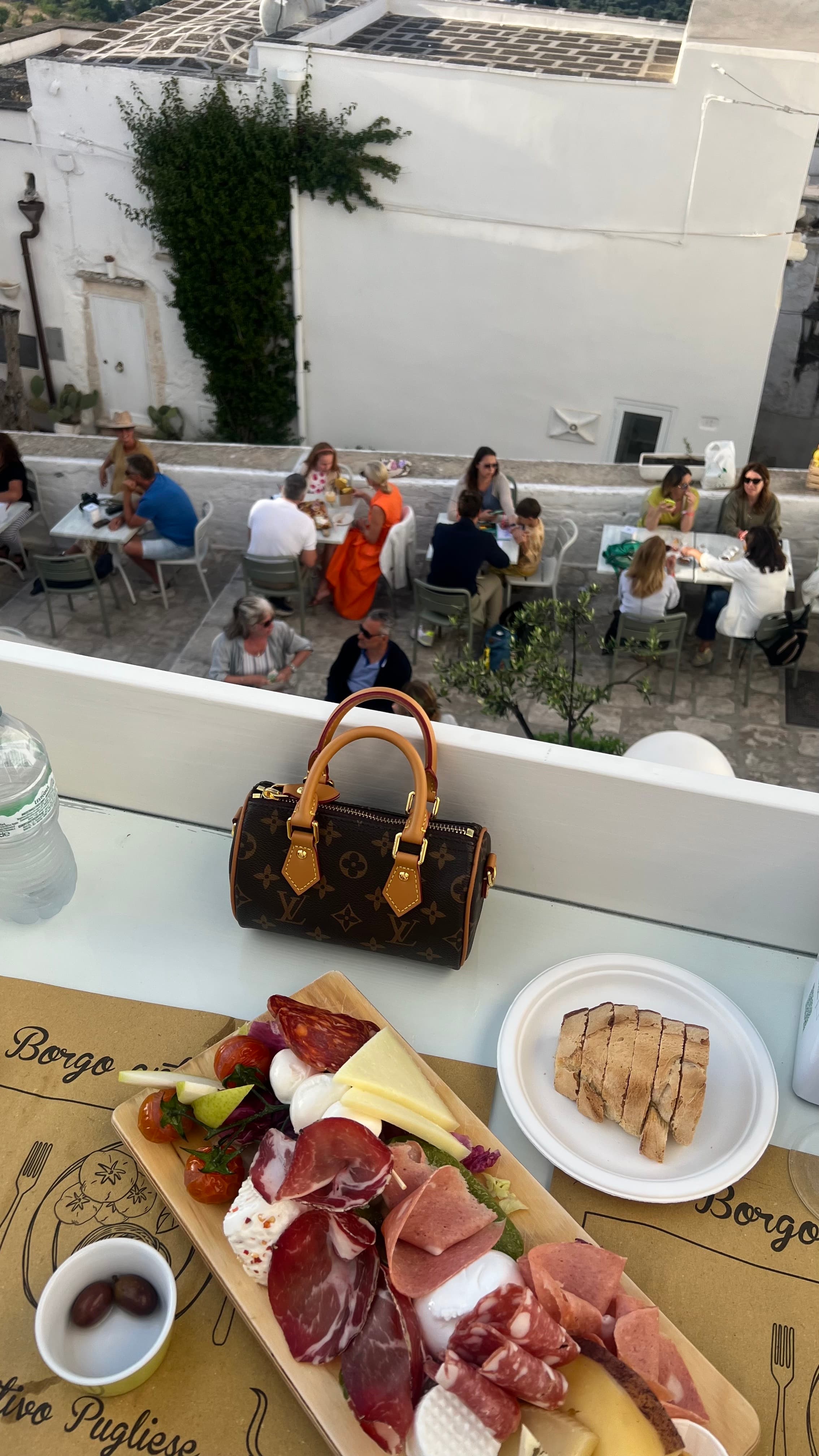 Plate of meats and cheese on a balcony overlooking the street below with people dining outdoors