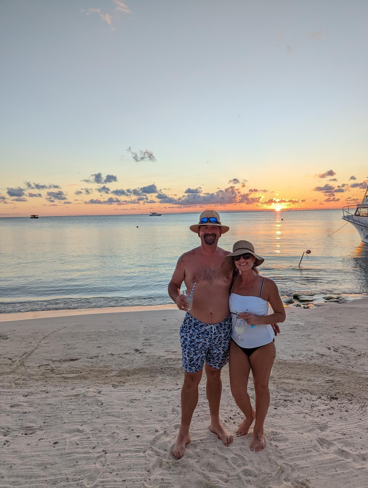 Advisor and a woman posing on a white sand beach with the sunset behind them.