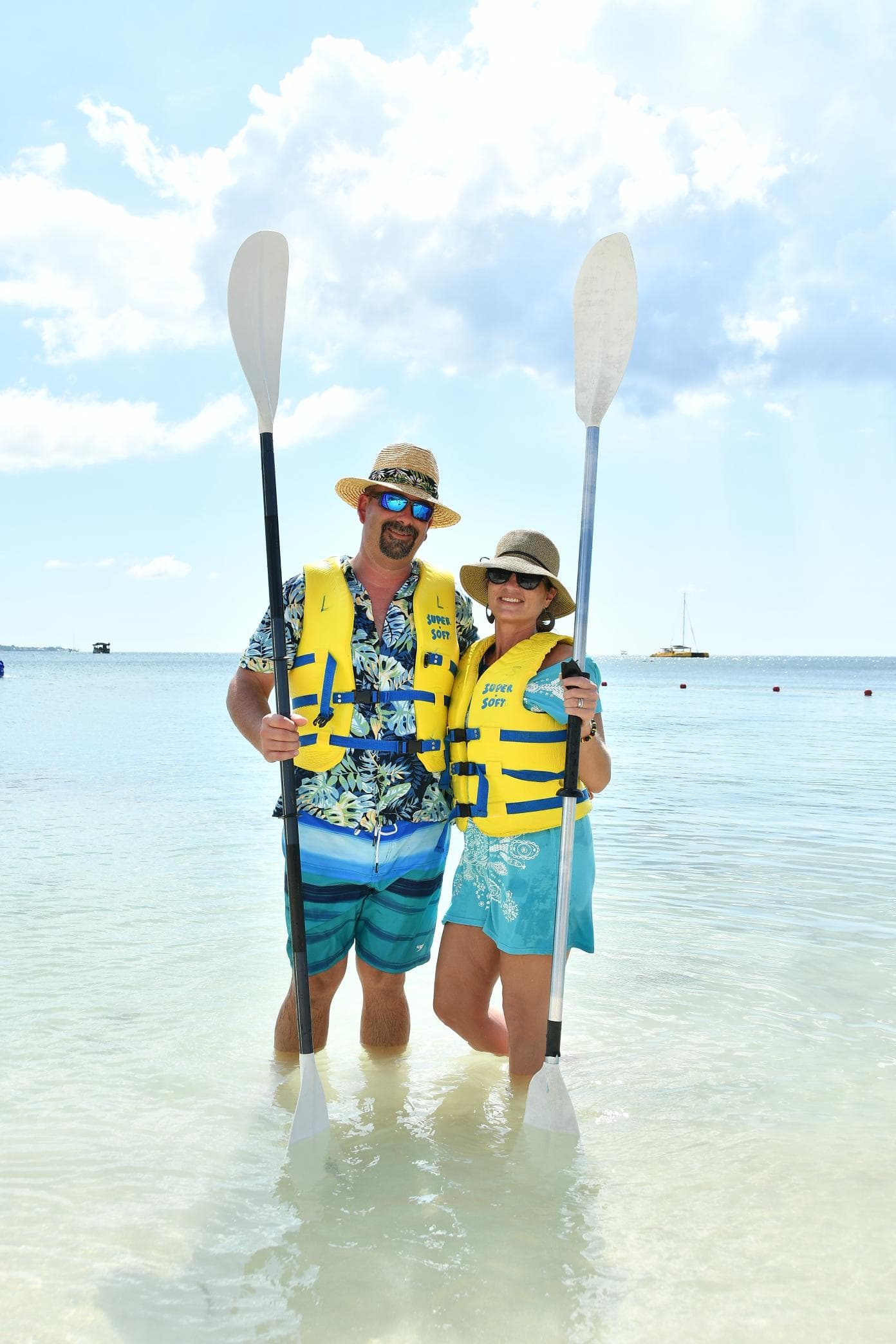 Advisor and a woman standing in the ocean wearing yellow life vests and holding oars on a sunny day.