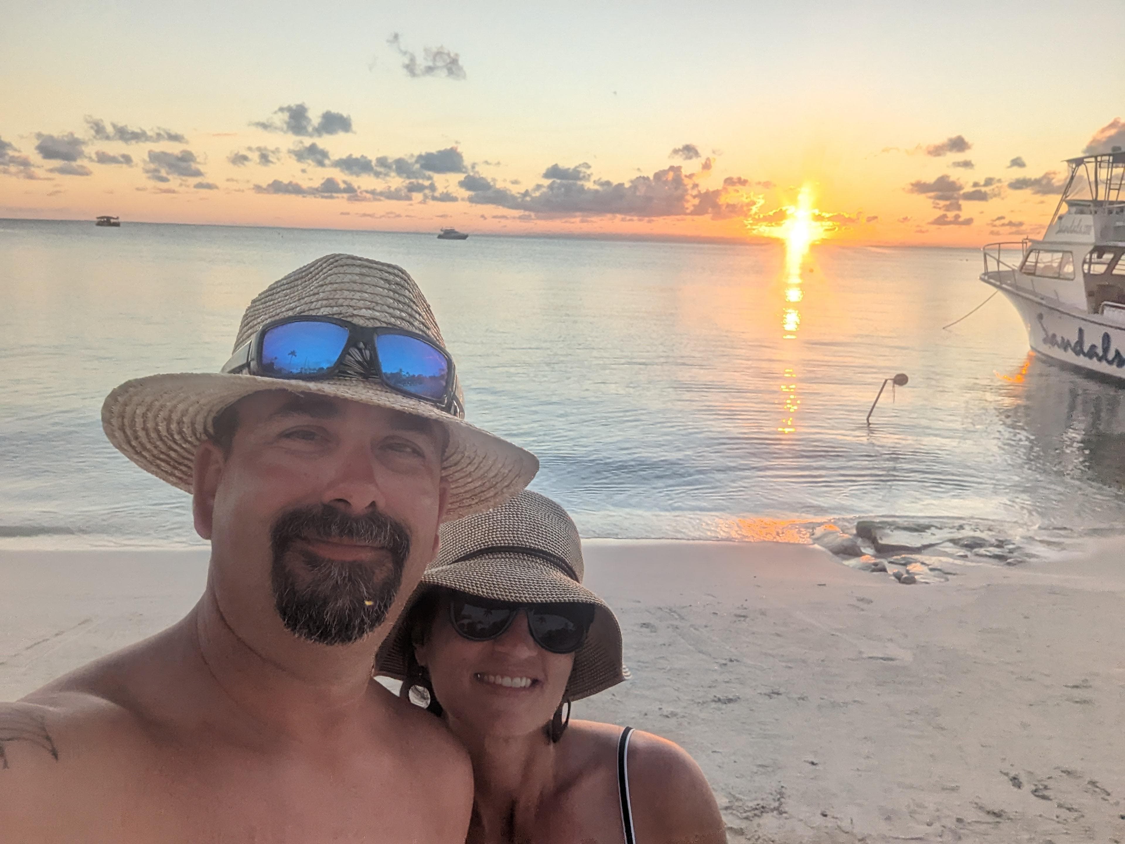 Advisor standing with a woman on the beach with a boat docked in the water behind them and the sun setting.