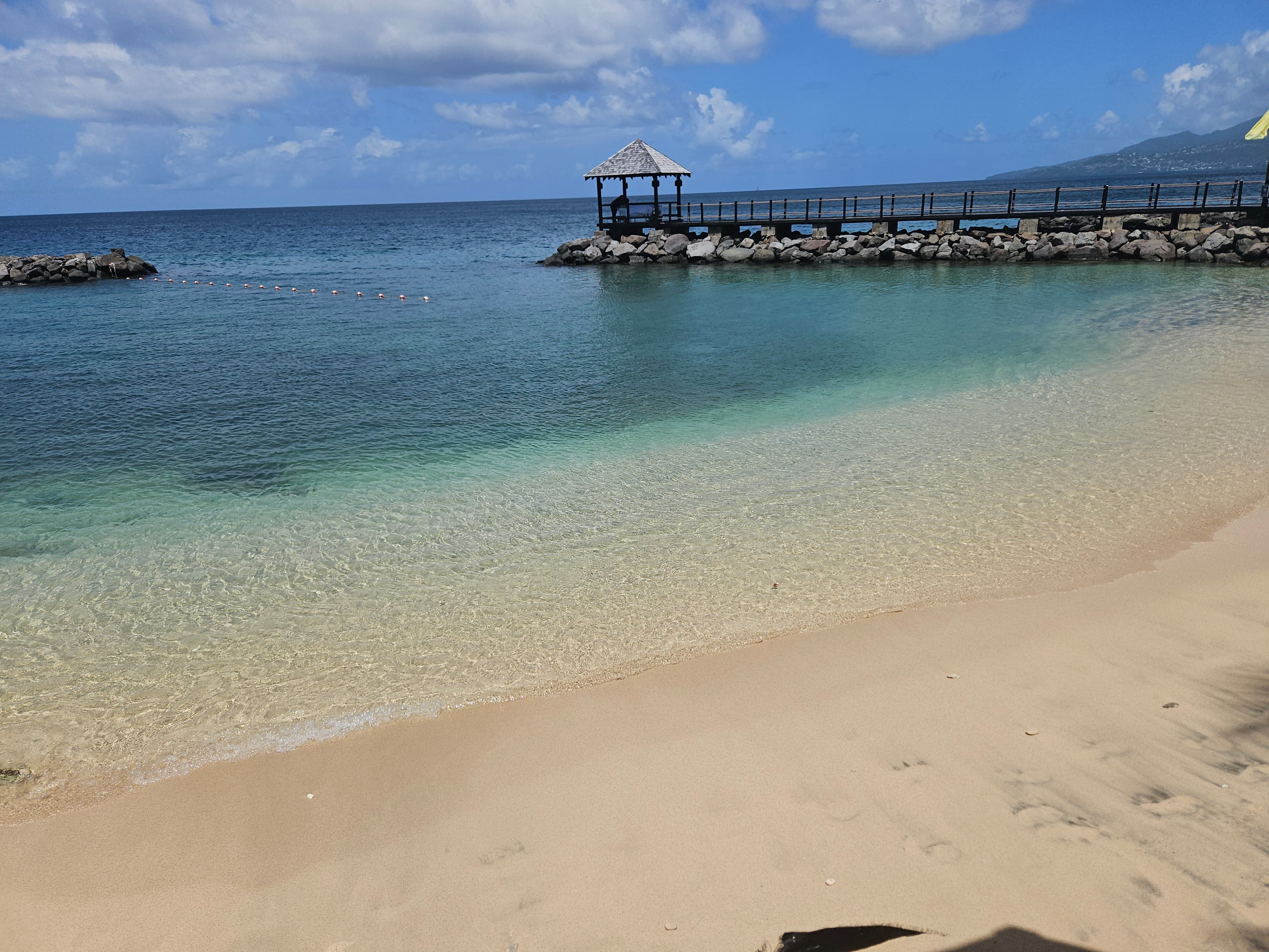 View of crystal clear ocean water with a pier in the distance on a sunny day