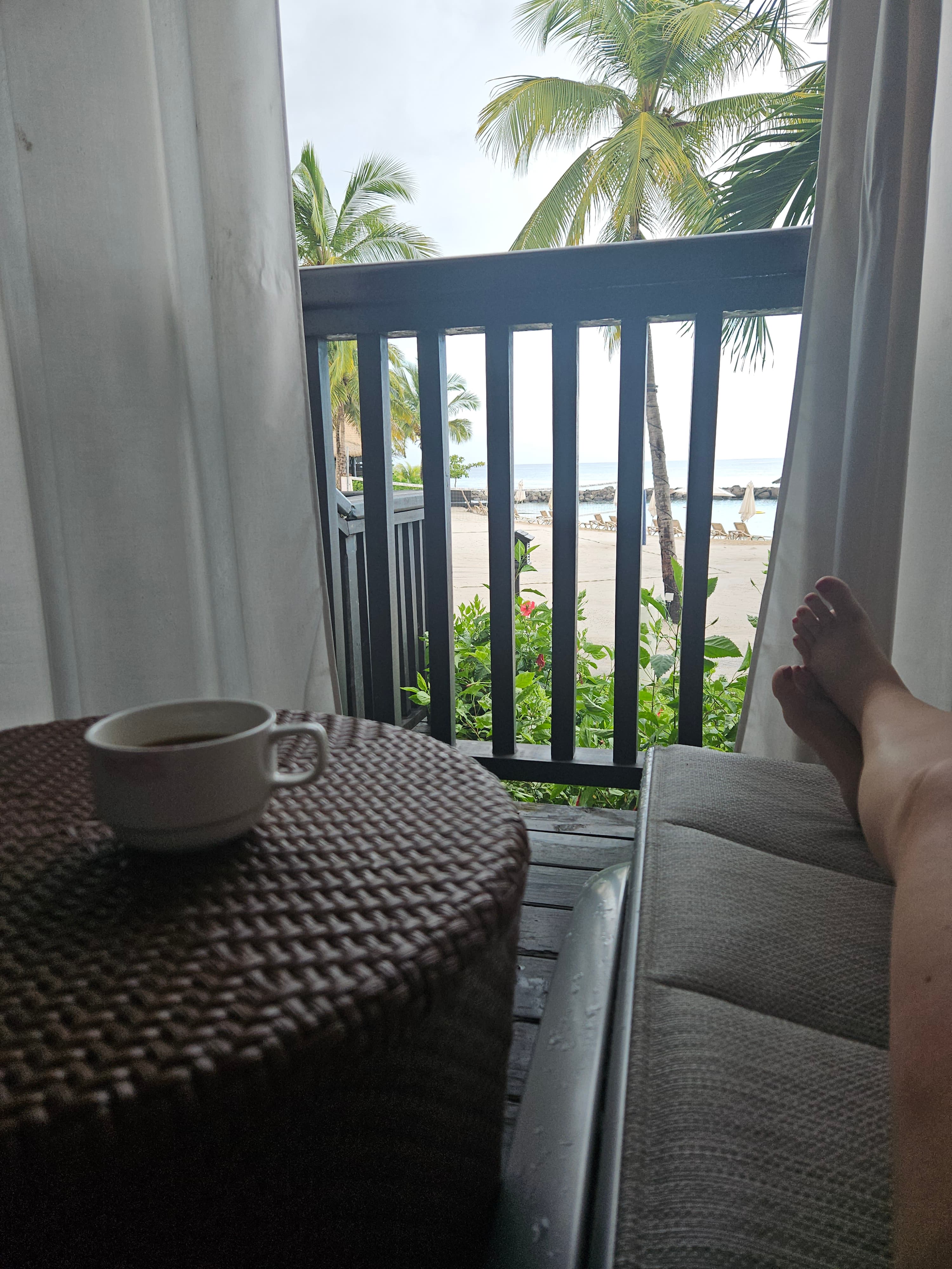 Advisor’s legs on a couch with a cup of coffee on the table beside her and palm trees visible outside the window