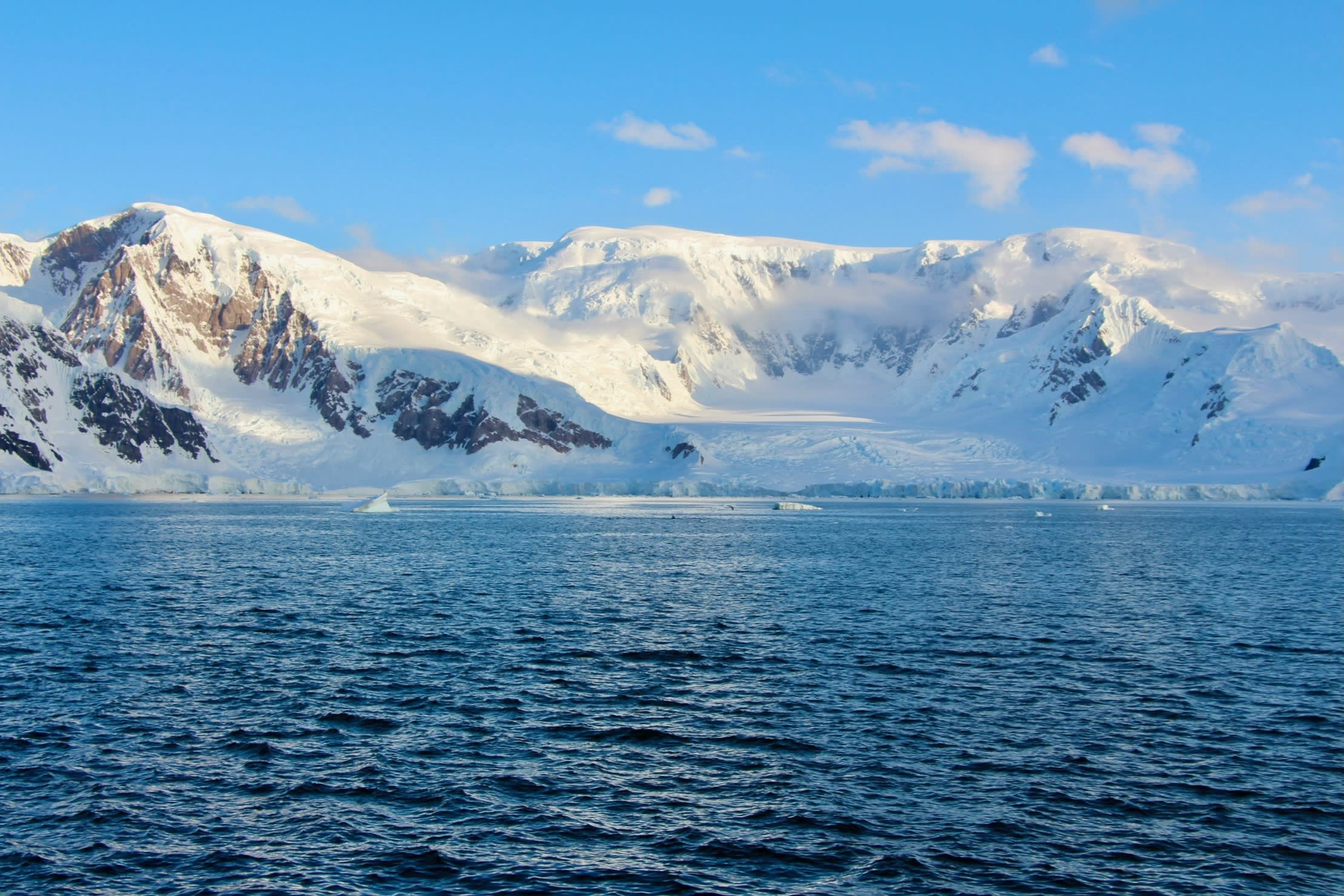 A beautiful view of a snow covered mountain range and rippling blue water.