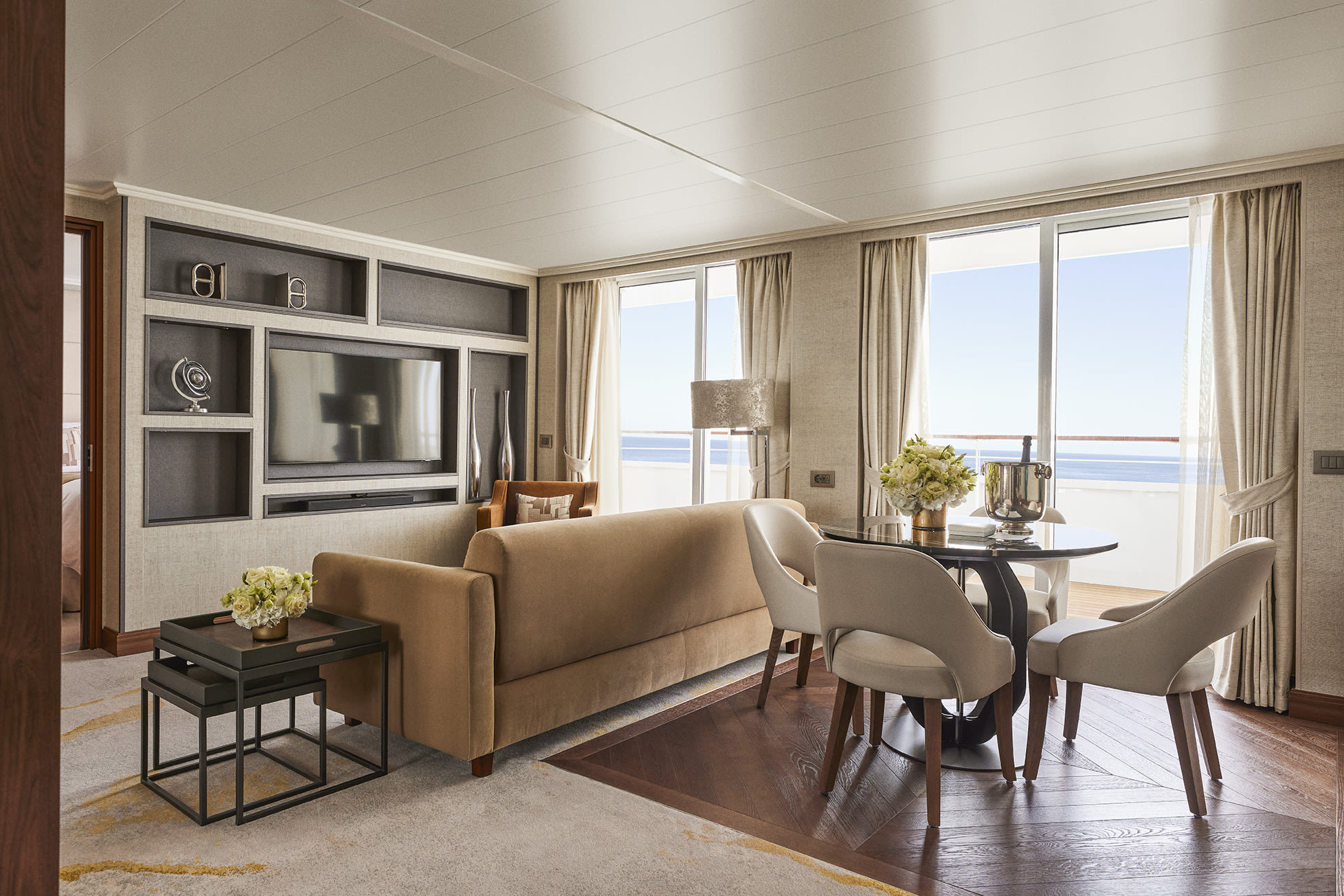 a luxe cruise living room with wooden floors and a balcony overlooking the ocean