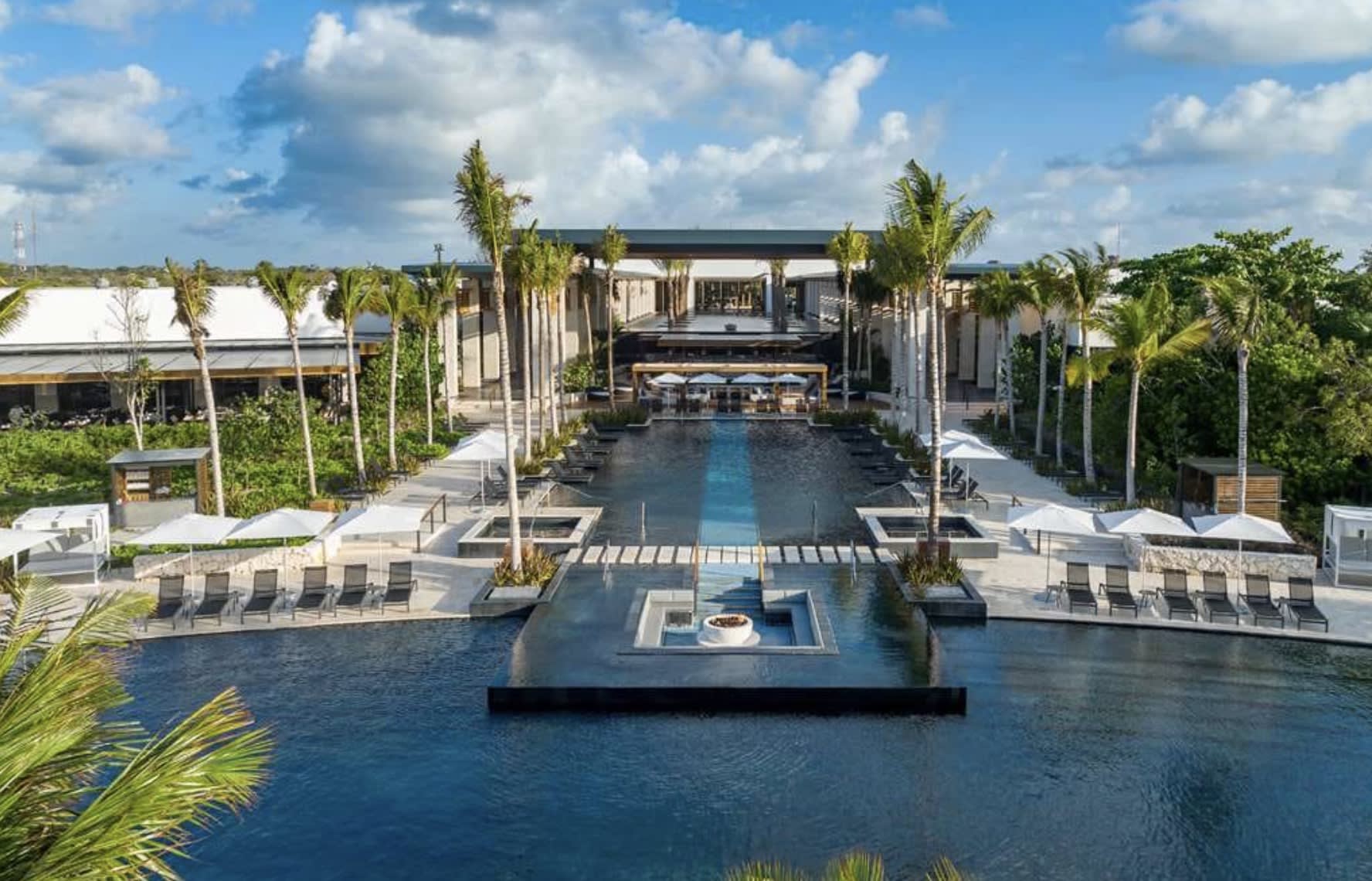 two pools surrounded by tall palm trees with a low-rise building in the background