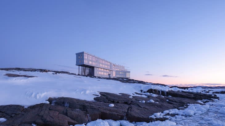 modern rectangular building set on a snowy cliff at sunset