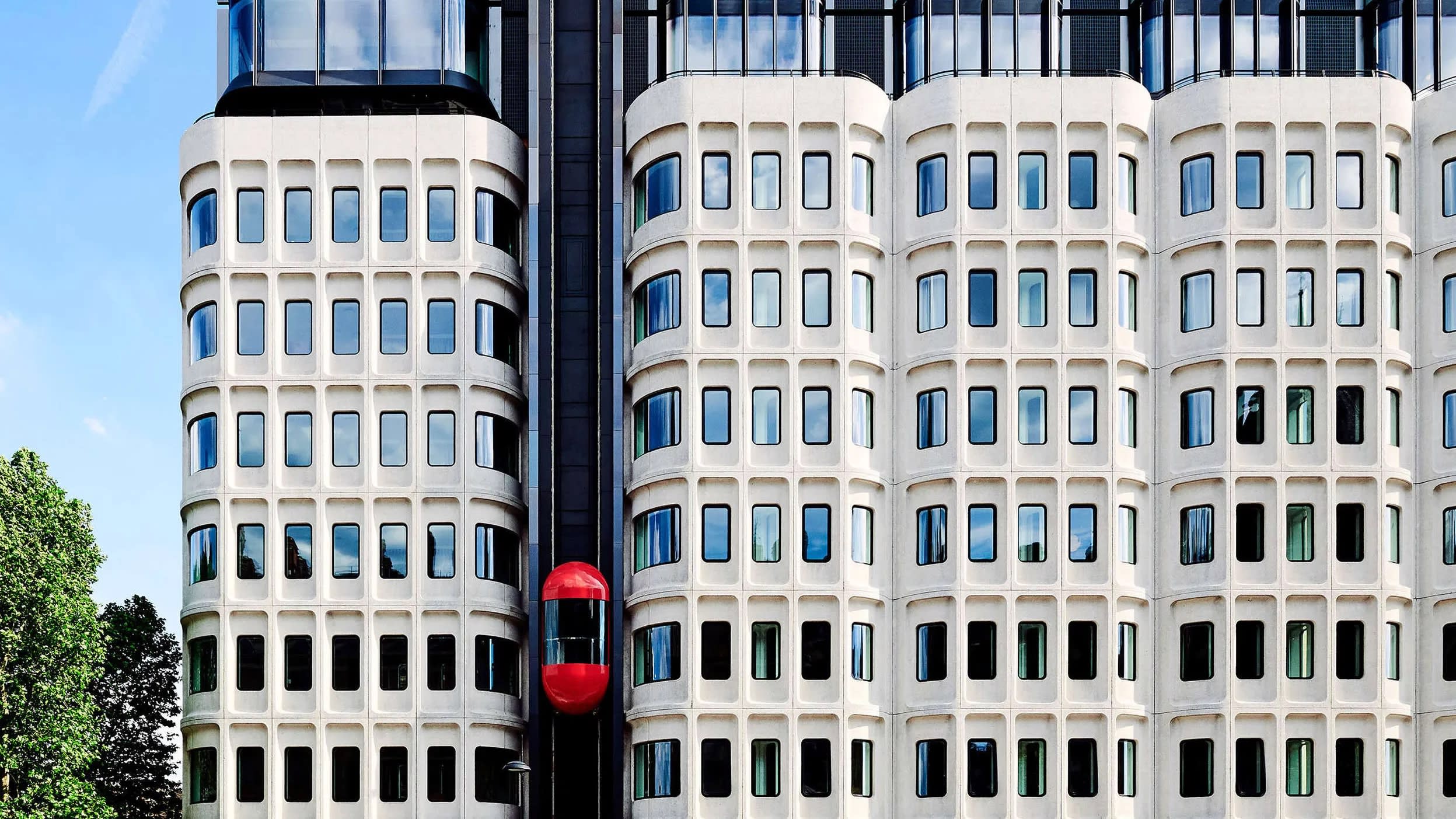 Building exterior with red pill-shaped elevator ascending up the facade.