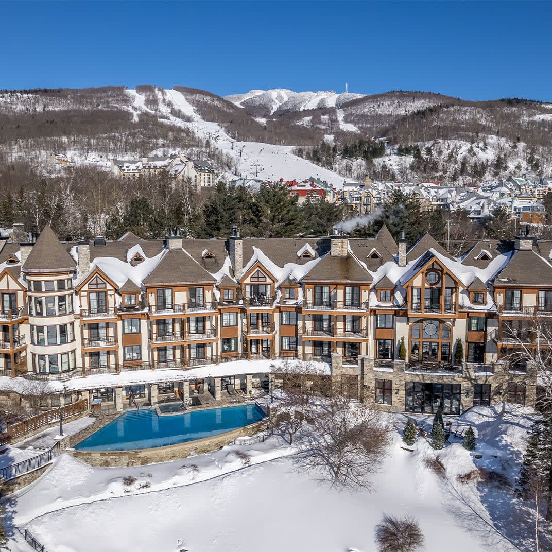A hotel with a pool out front surrounded by snowy grounds and mountains in the background
