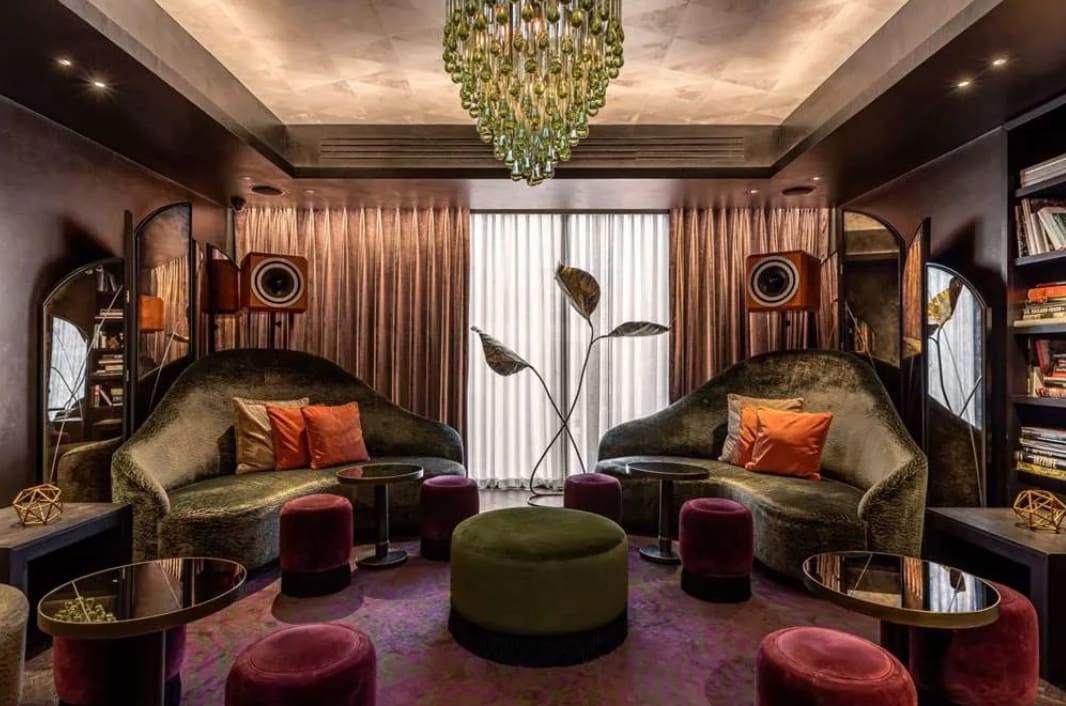 Eclectic, plush lounge area with purple carpet, olive green sofas and orange cushions.