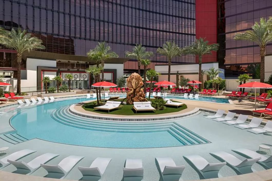 Modern hotel pool area with white sun loungers and red umbrellas