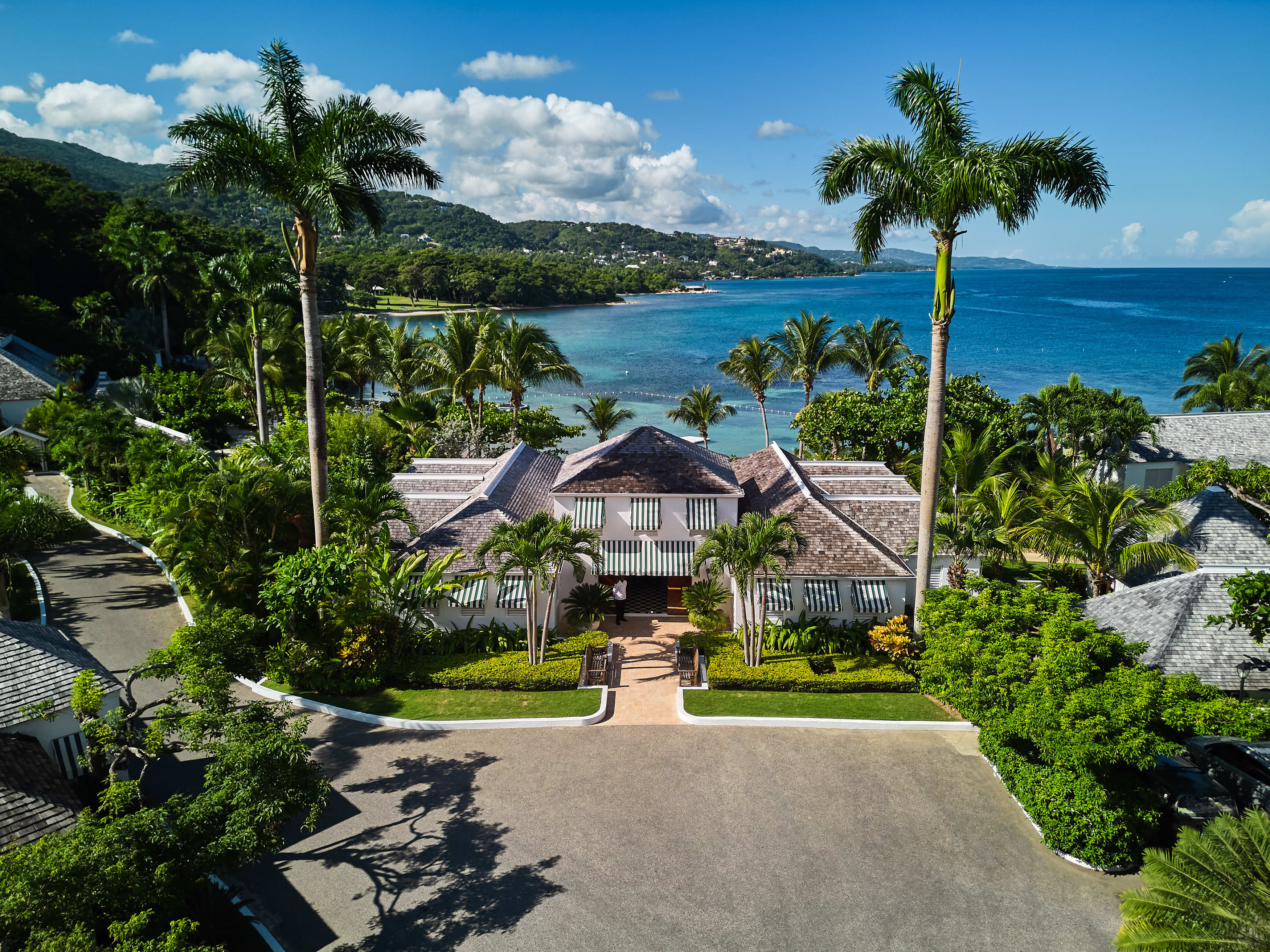 An aerial view of the entrance of a hotel with palm trees and ocean backdrop