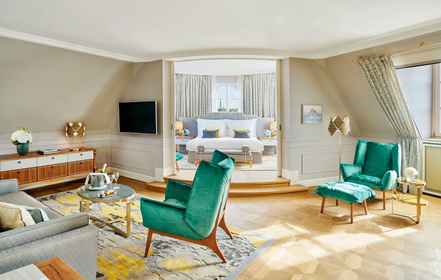 An elegant suite with emerald green armchairs, neutral colored furnishings and a separate bedroom