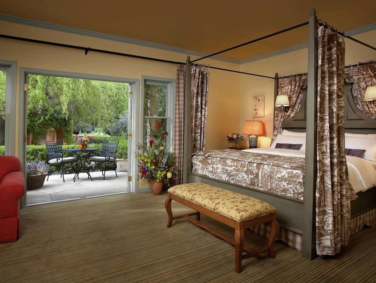 Hotel suite interior with four-poster bed and balcony with outdoor seating and garden view