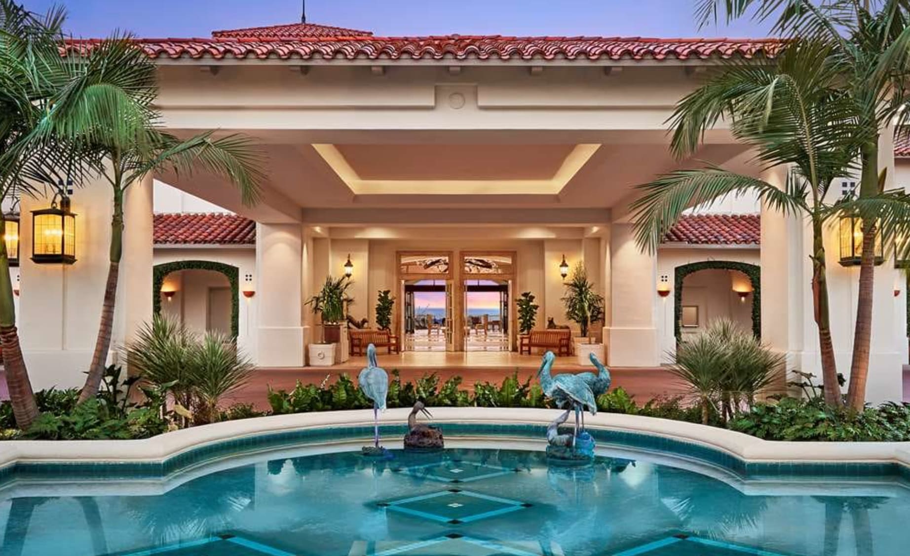 Hotel entrance with pillars and small fountain pool and ocean in the distance