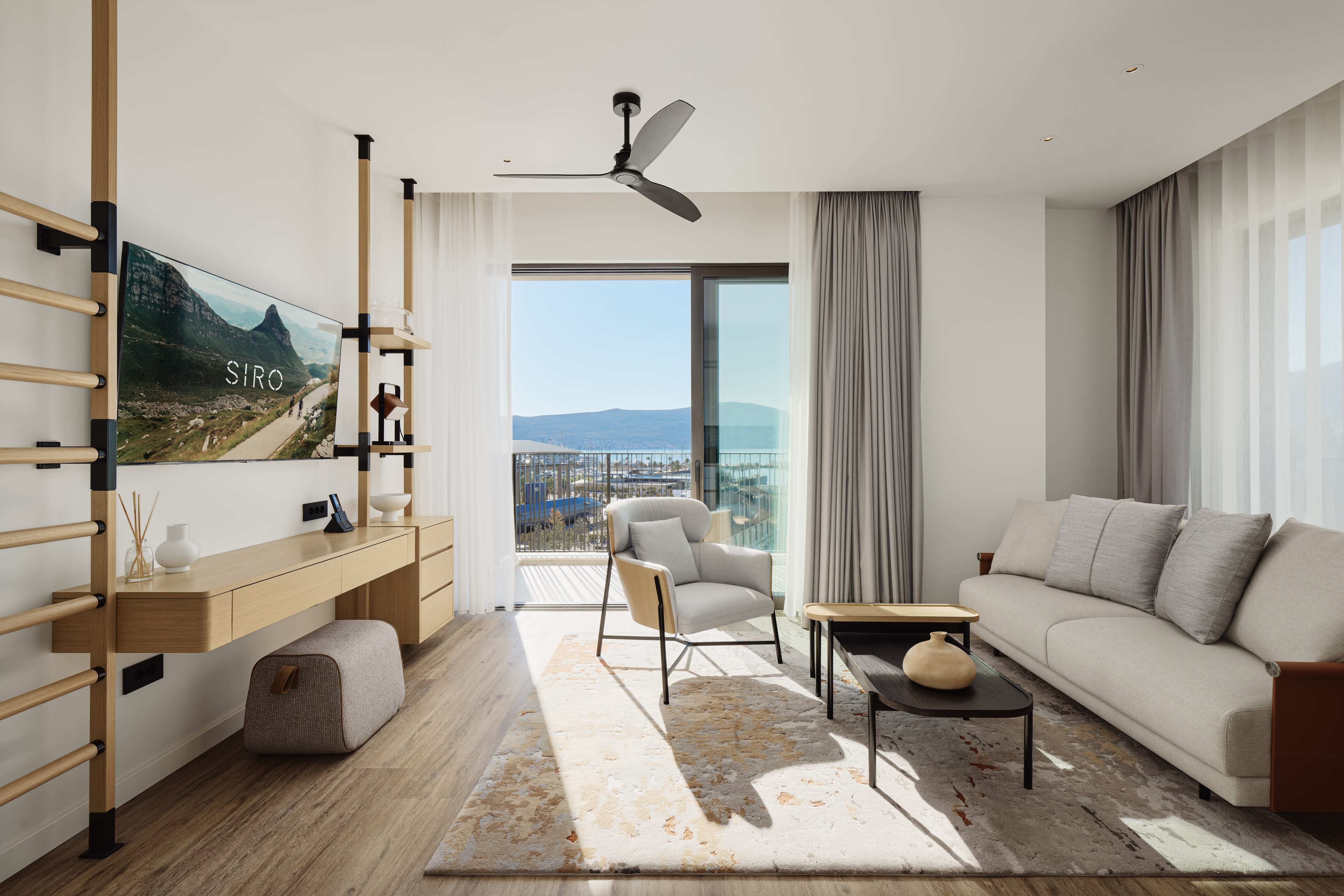 A hotel living room with natural sunlight coming through the open balcony door