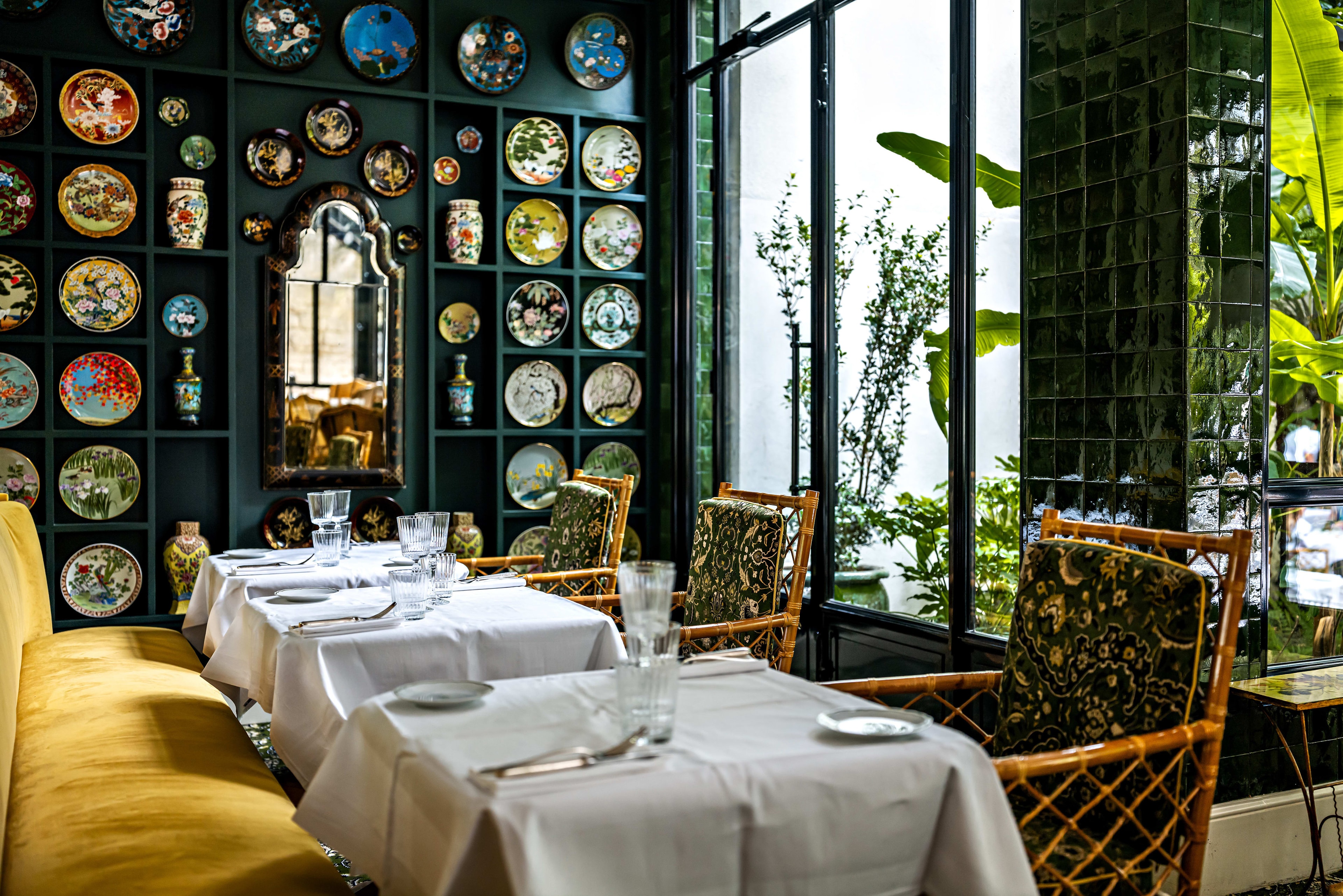 A hotel dining area with colorful round plates on the wall, dark green walls, yellow seating and white tablecloths.