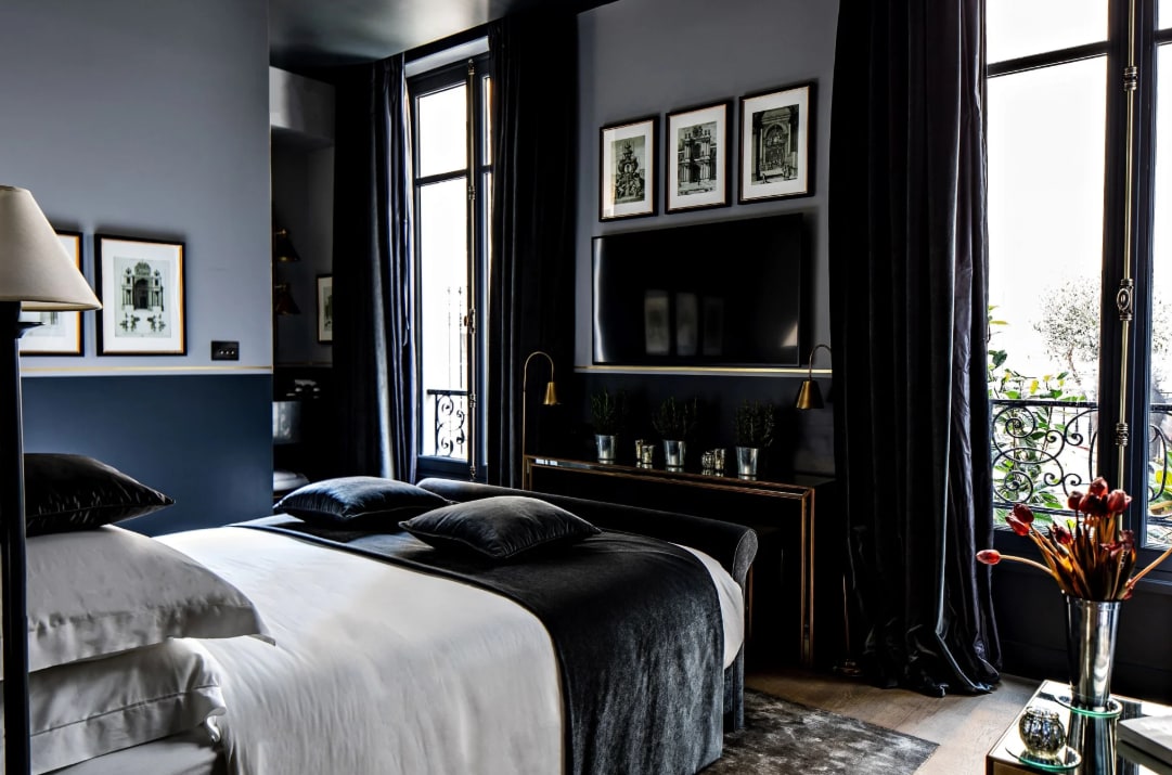 A hotel room feauturing dark walls, plush furnishings and velvet drapes with moody lighting.