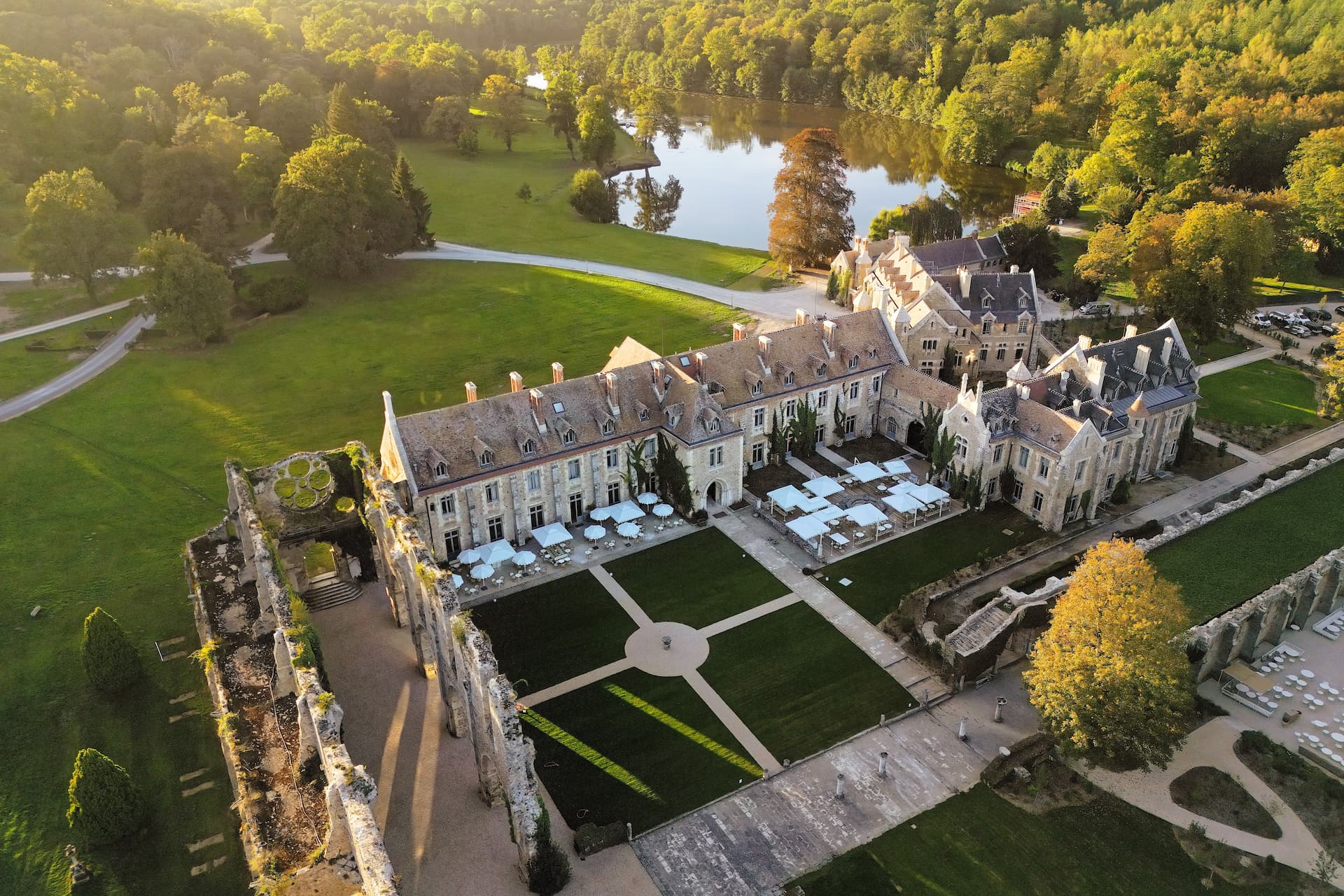 An aerial view of a historic building partly in ruins with green gardens and a lake in the background surrounded by forest