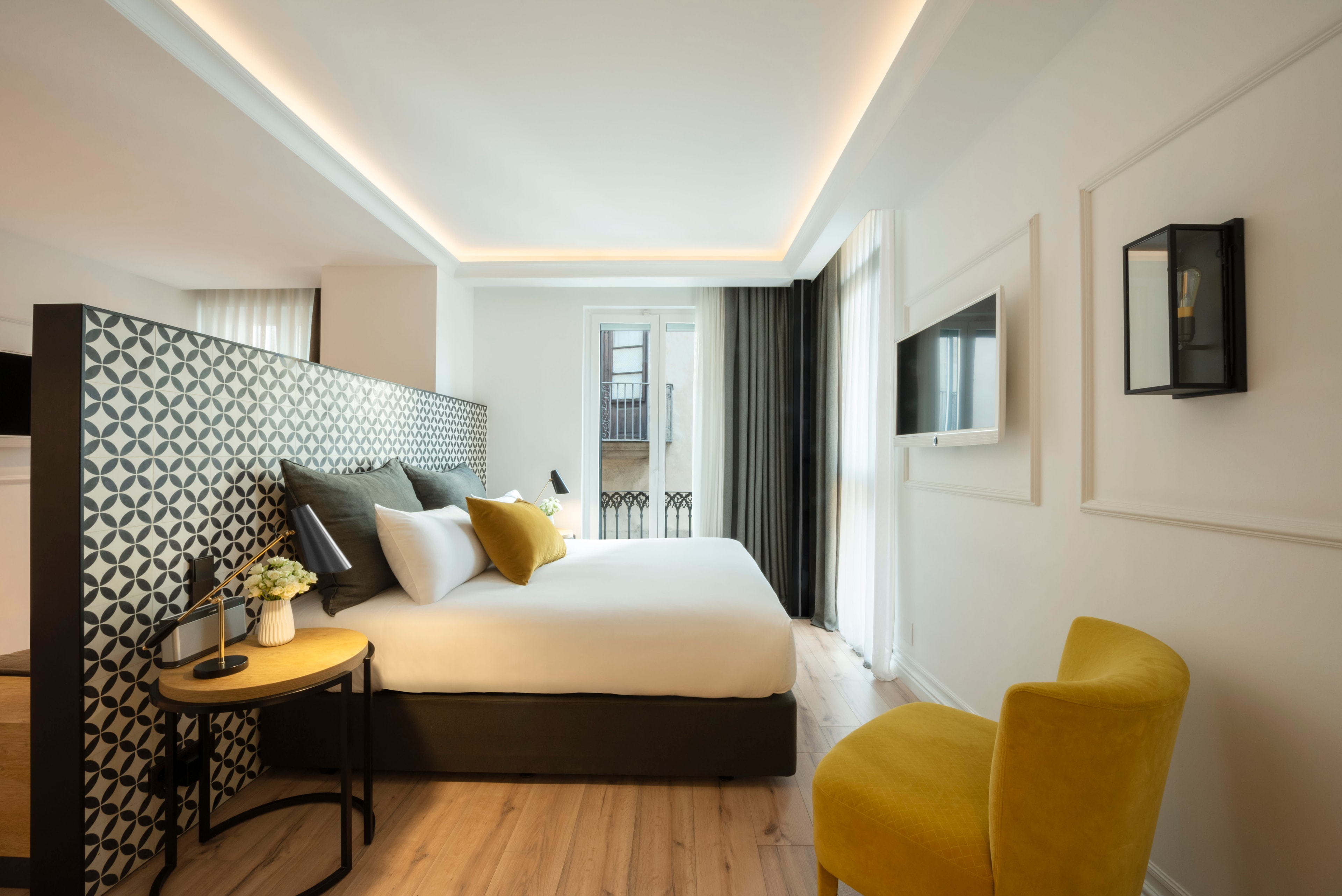 A modern suite with wood flooring, yellow armchair and black and white bed and fixtures