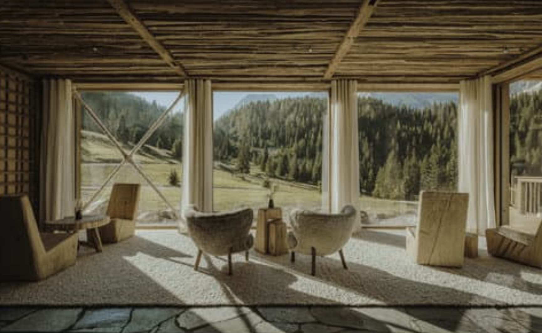 A living space a rustic but modern chalet asthetic with floor-to-ceiling windows looking out onto lush greenery