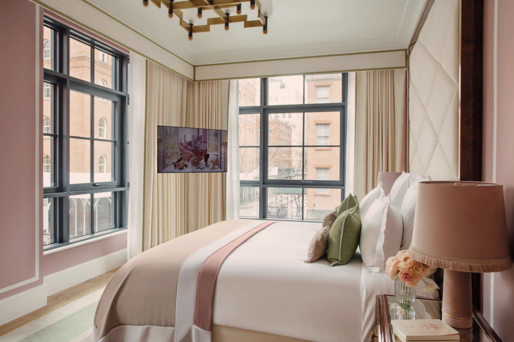An elegant hotel room in pastel pink tones looking out onto New York buildings