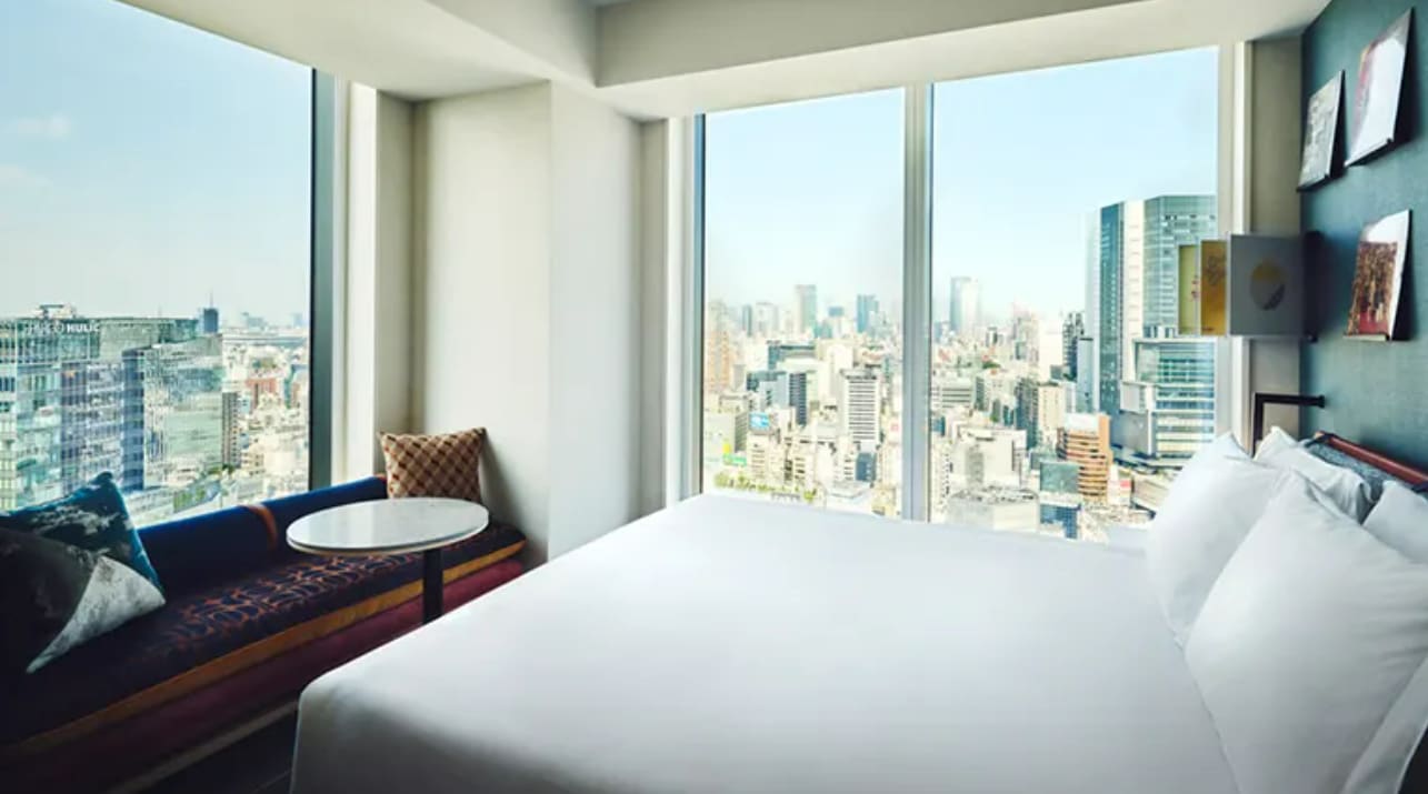 A hotel room with large windows and cityscape views on a high floor
