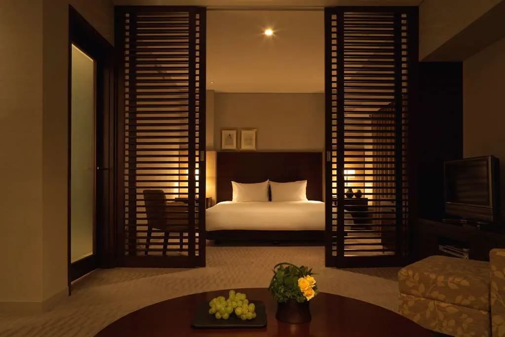 A dimly light hotel room with wooden sliding door with slats and neutral tones