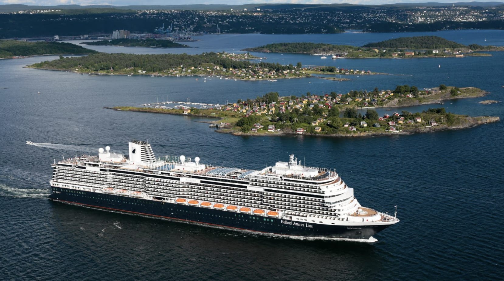 An aerial view of a cruise ship sailing on rich blue waters with harbors and land in the surrounding area