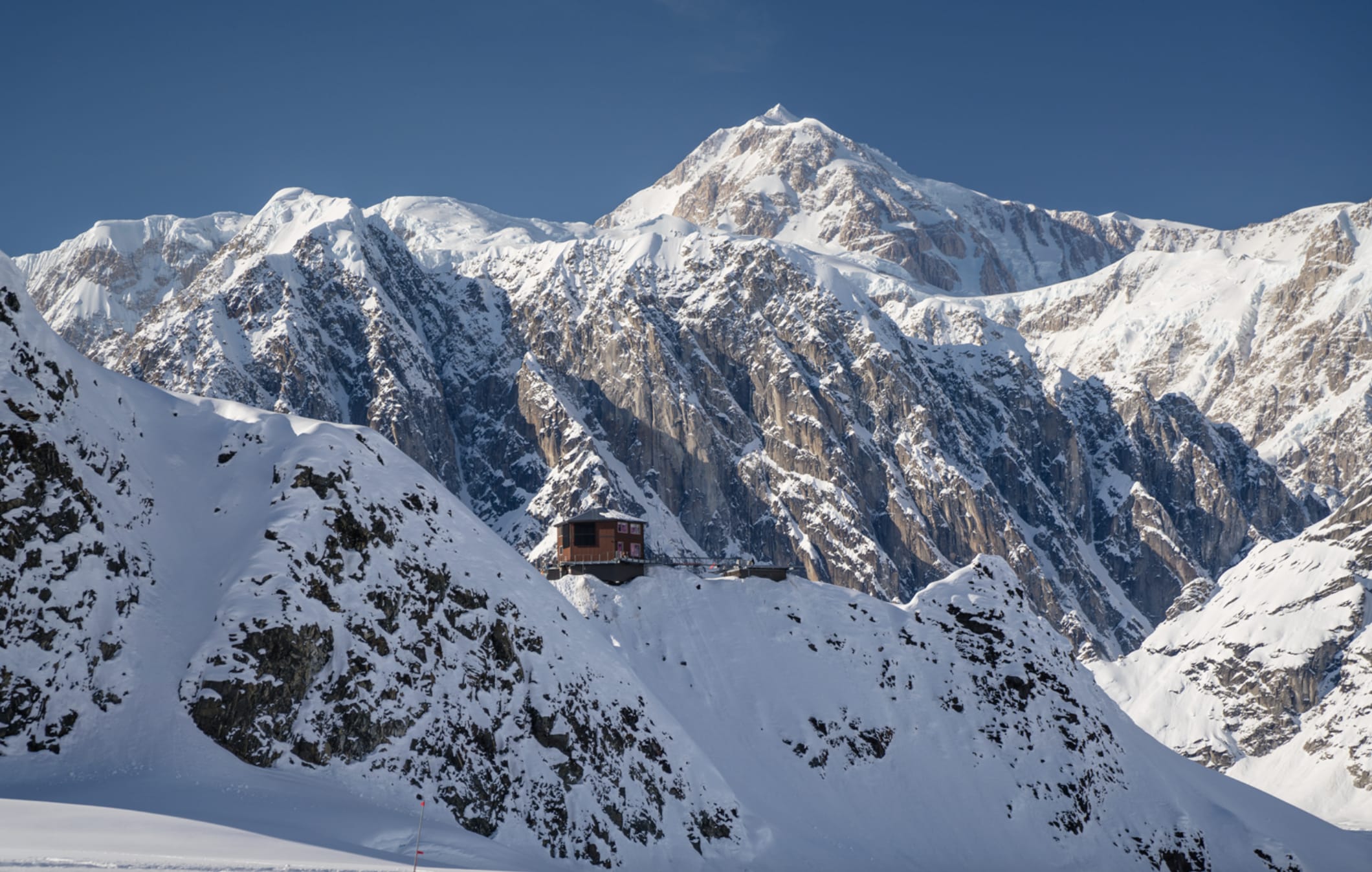 A view of snow covered mountains and a small hut nestled on top of a cliff