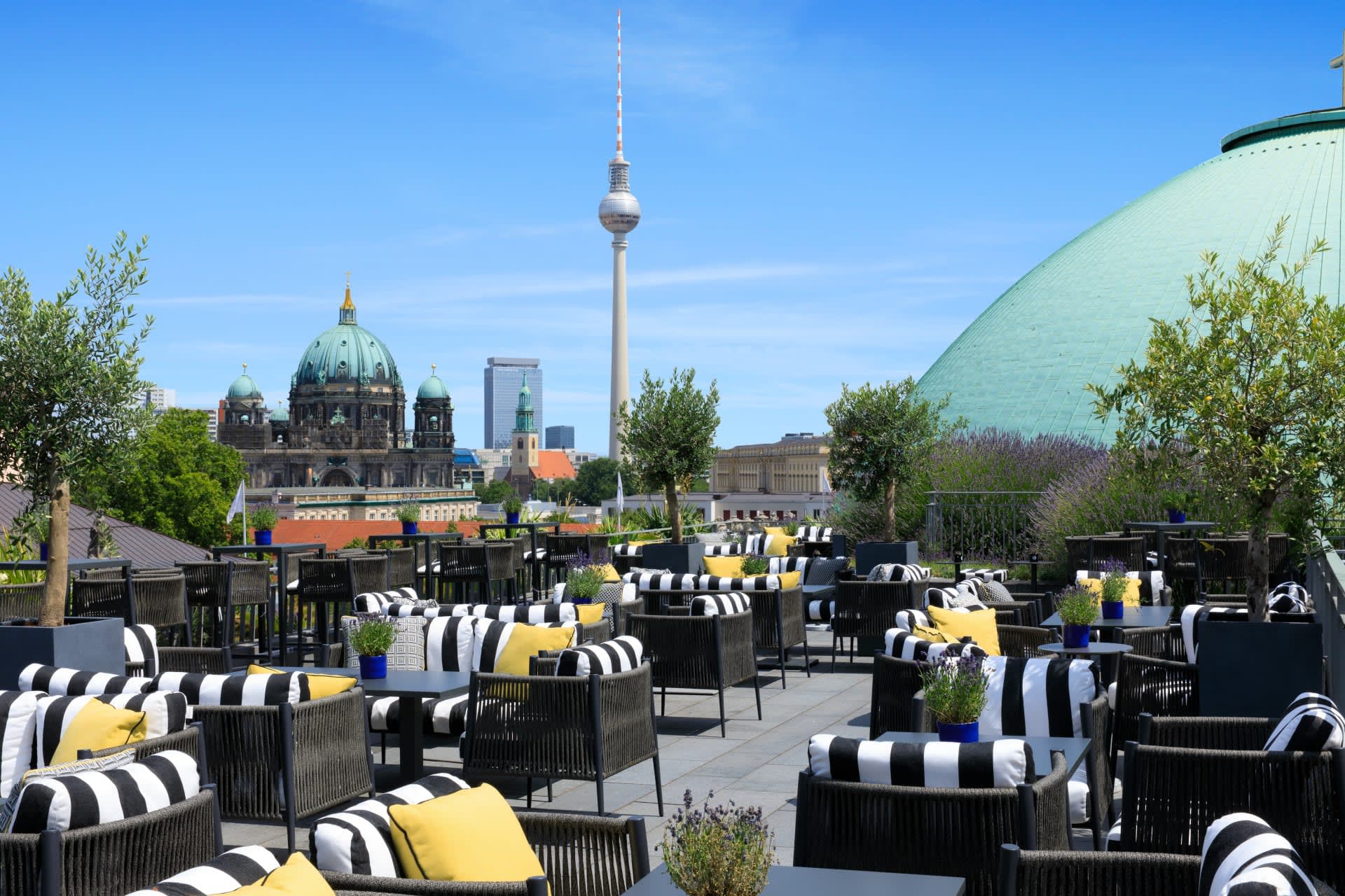 An outdoor patio with black chairs, white and black stripe cushions with yellow pillows, with a skyscraper and green domed buildings in the background