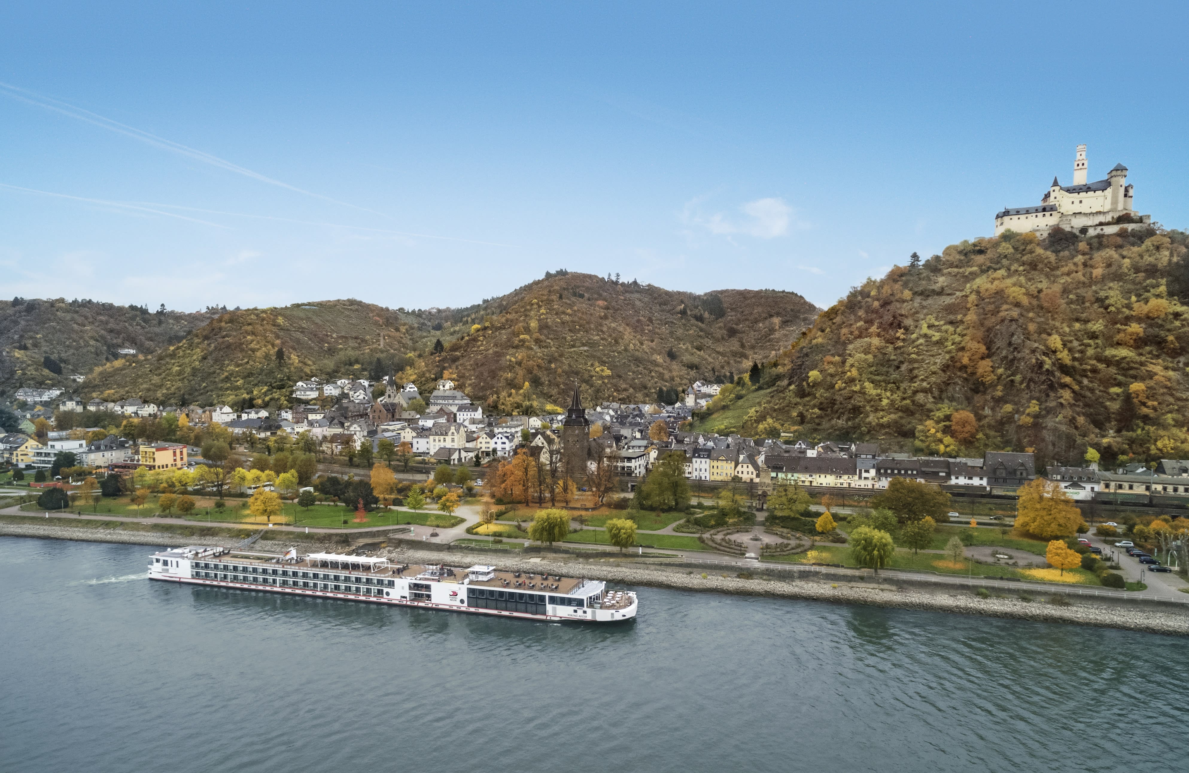 A river cruise boat in the foreground with a town behind it at the base of a hill with a castle on top