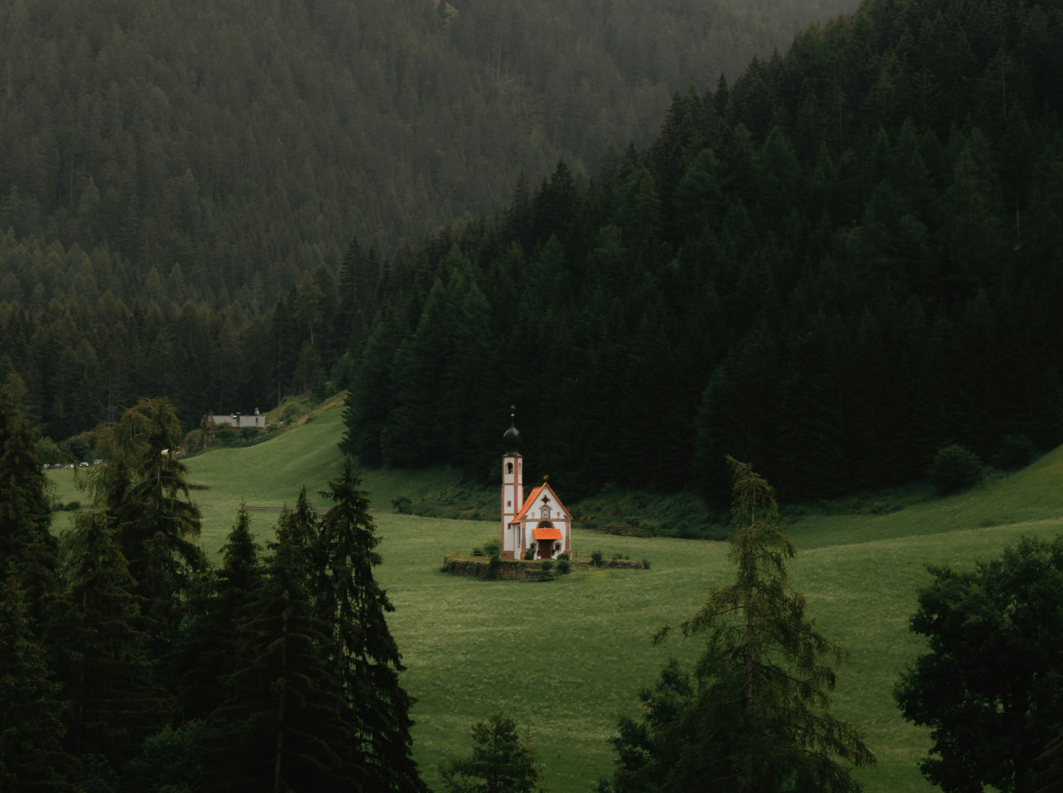 A white church in the middle of a green field with green trees and hills all around