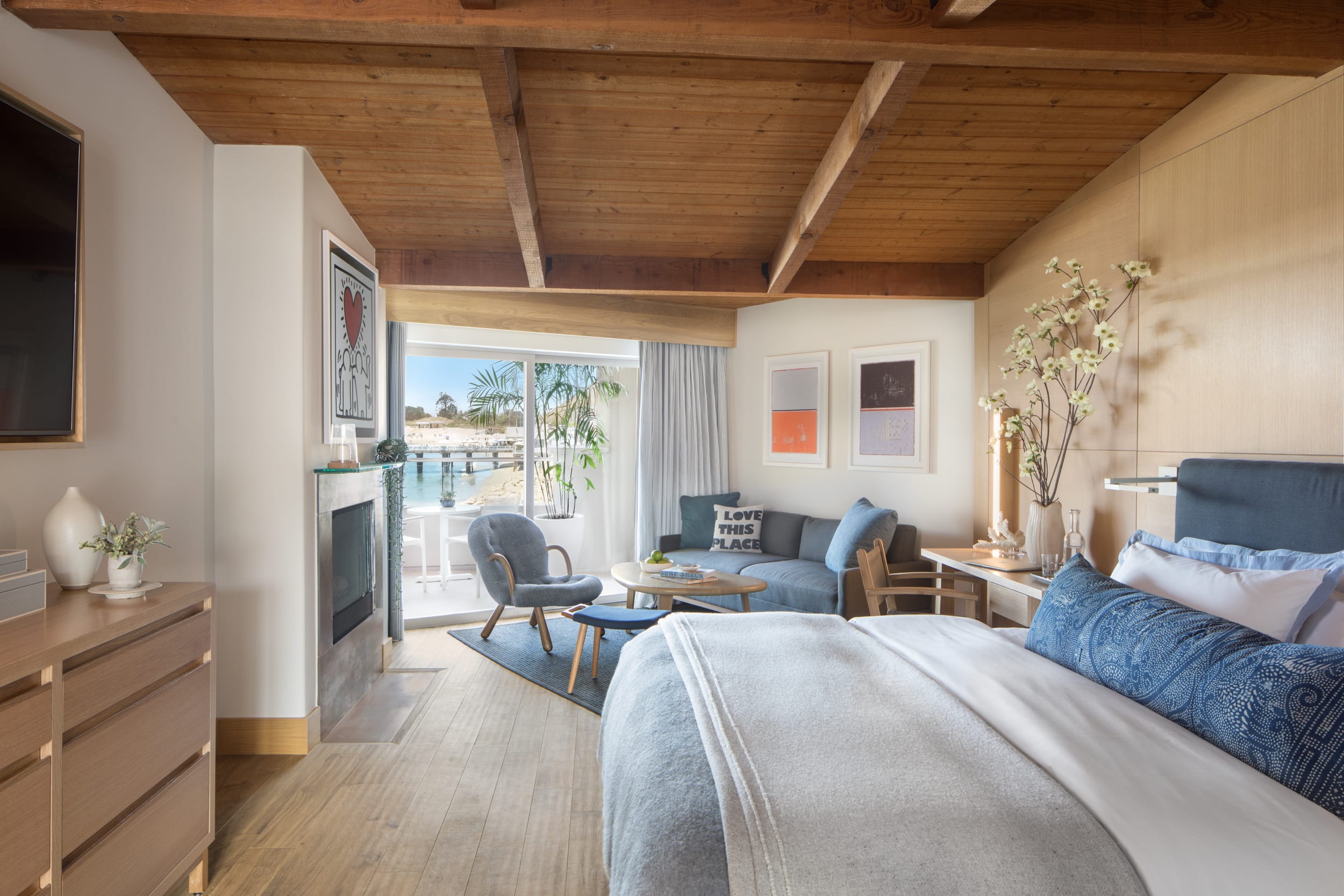 A hotel room with wooden beams and a coastal vibe with white and blue decor and sea views in the background