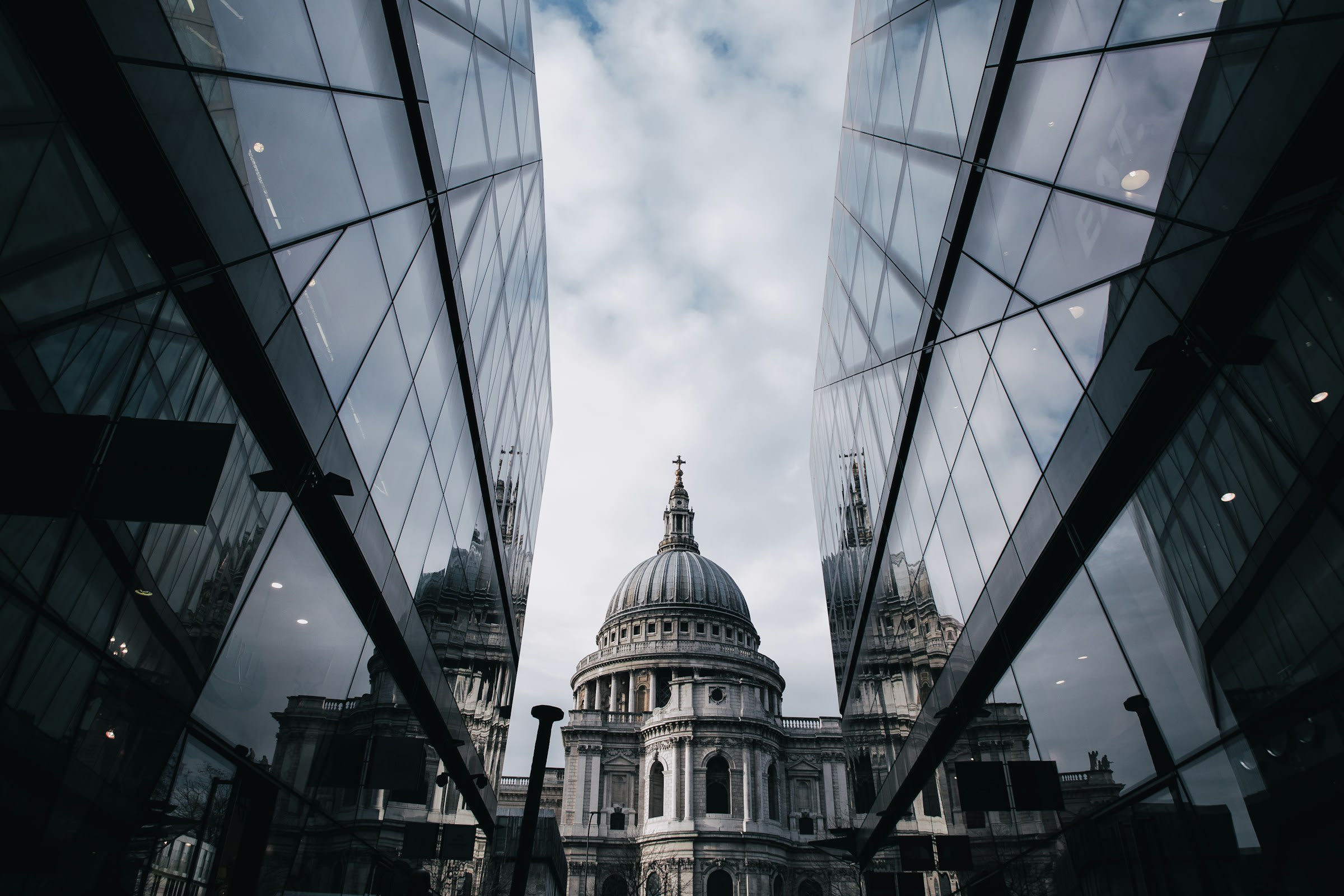 Glass skyscrapers framing the dome of a cathedral beneath a cloudy sky during daytime