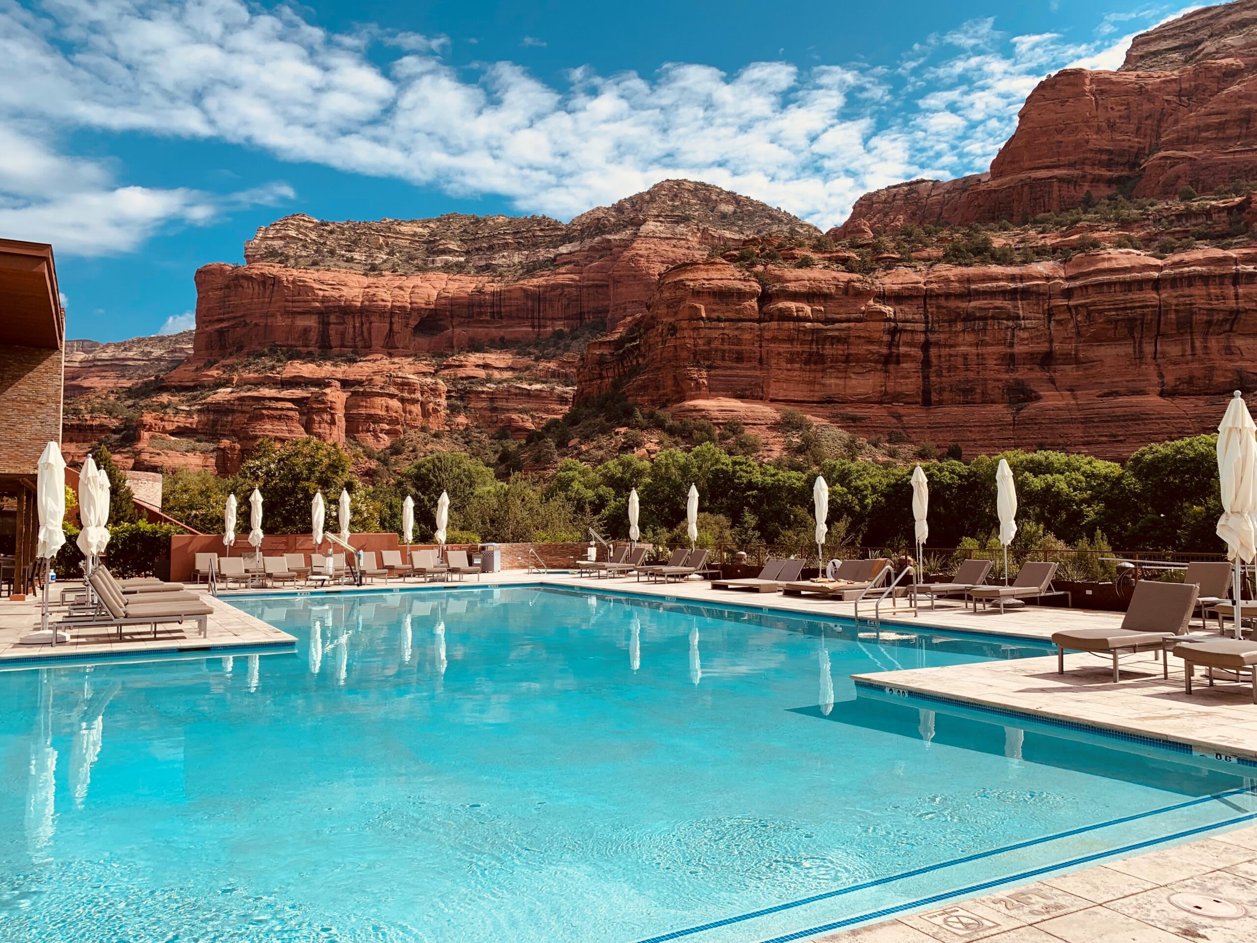 a pool surrounded by chaise lounges and red rock cliffs behind