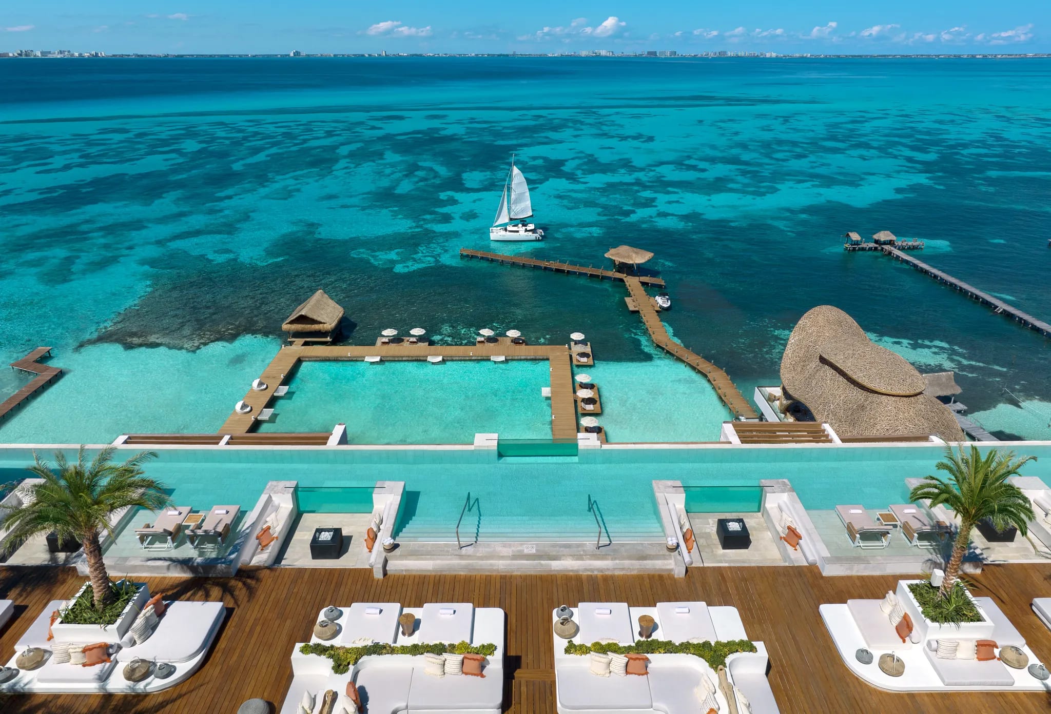 Aerial view of a rooftop infinity pool overlooking turquoise ocean waters with docks and a sailboat