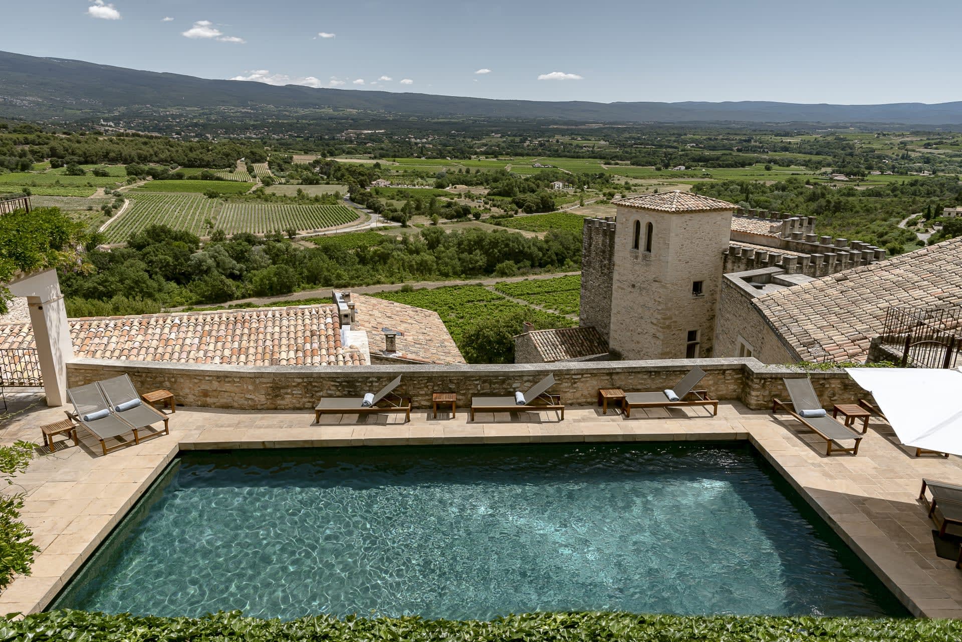 Aerial view of a rooftop pool on a restored tan stone building with green landscape behind