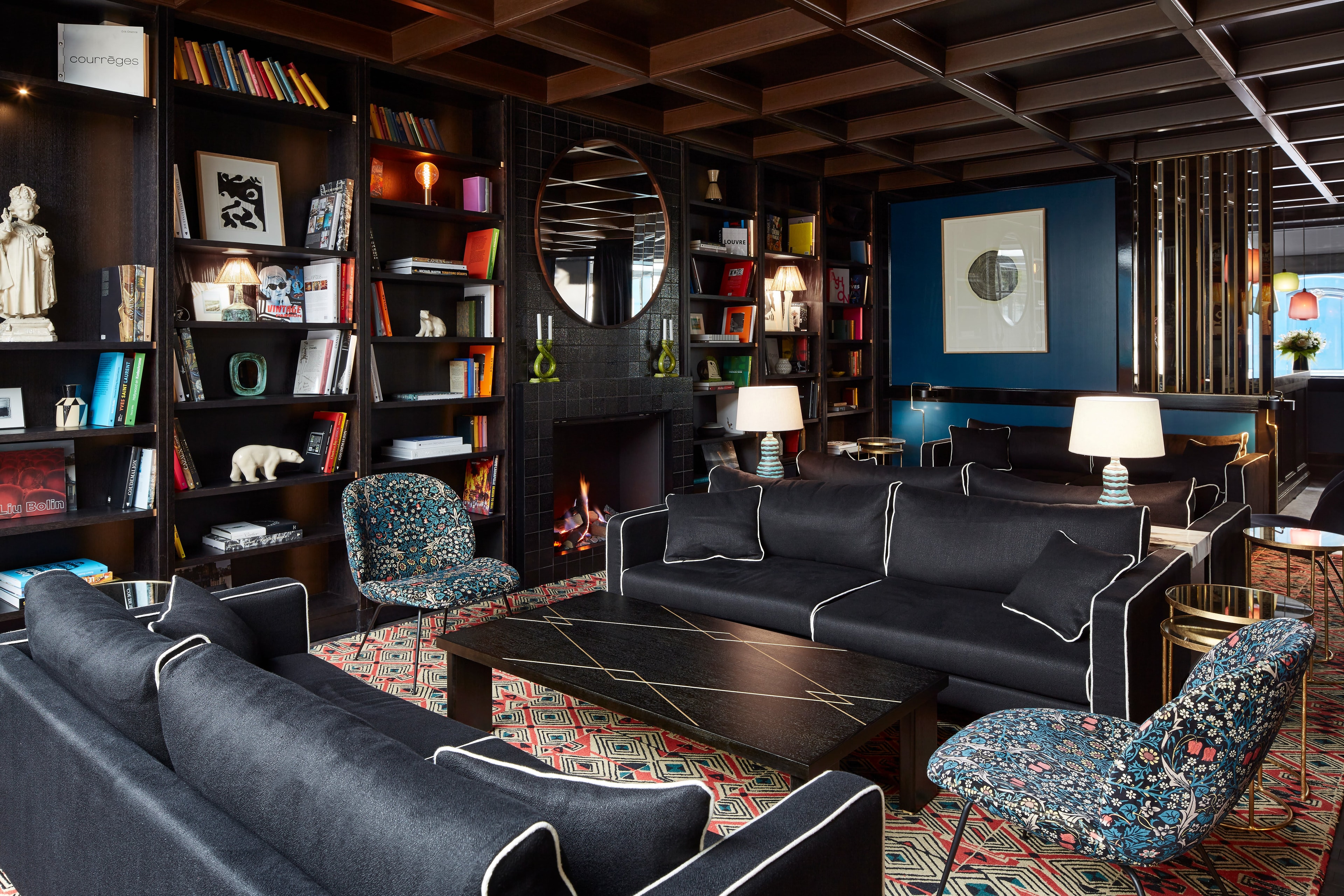A cozy hotel lounge with floor-to-ceiling bookshelves and dark furnishings and walls
