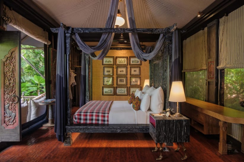 A bed beneath black canopy bed in a brown room with pictures on the wall