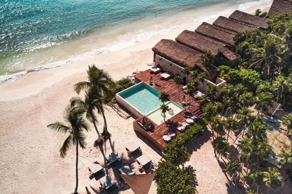 Aerial view of beach and turquoise ocean with palm trees and cabanas with a pool