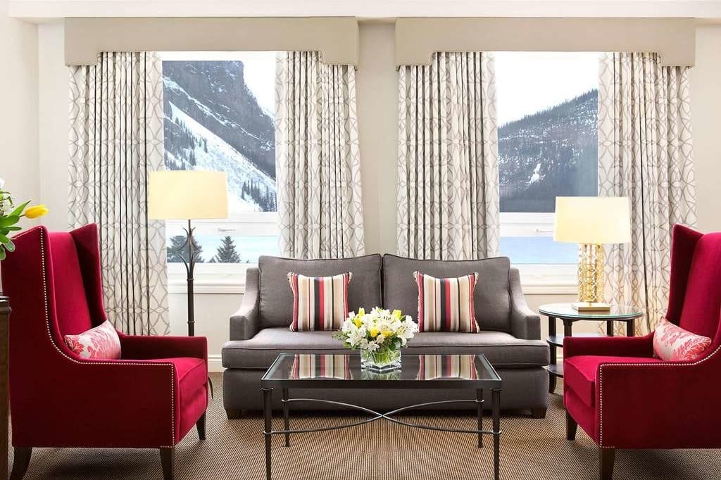 two red upholstered chairs in a hotel living room overlooking an alpine lake